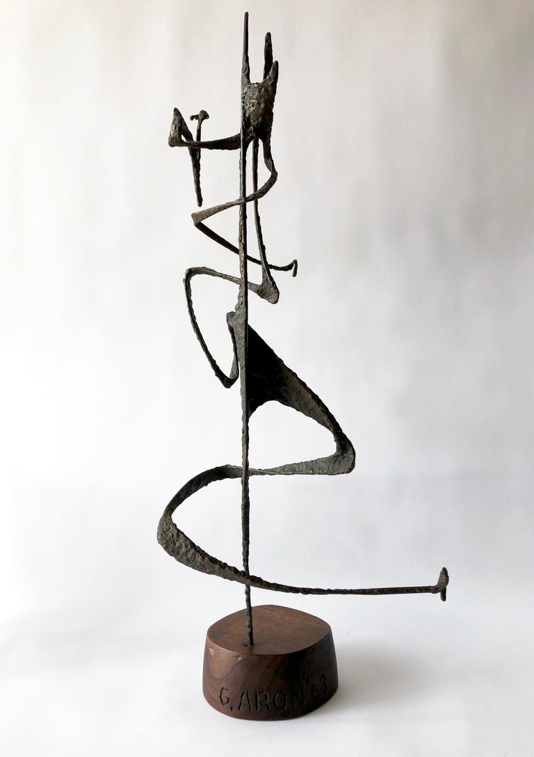 Abstract modernist iron sculpture on wood base created by artist G. Aron and dated 63. Sculpture has fluid lines and appears as if the piece should have kinetic movement. It measures 27.5