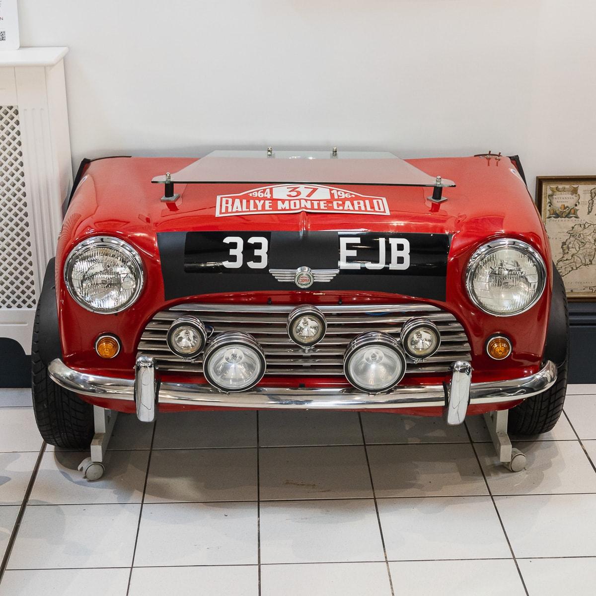 An Unusual 1964 Monte Carlo Rally Replica Mini Front End, in the form of a desk (modern), with glass shelf and a speedometer converted to a clock, the head lamps electrified, on a metal frame with castors. The desk design is based on Paddy Hopkirk's