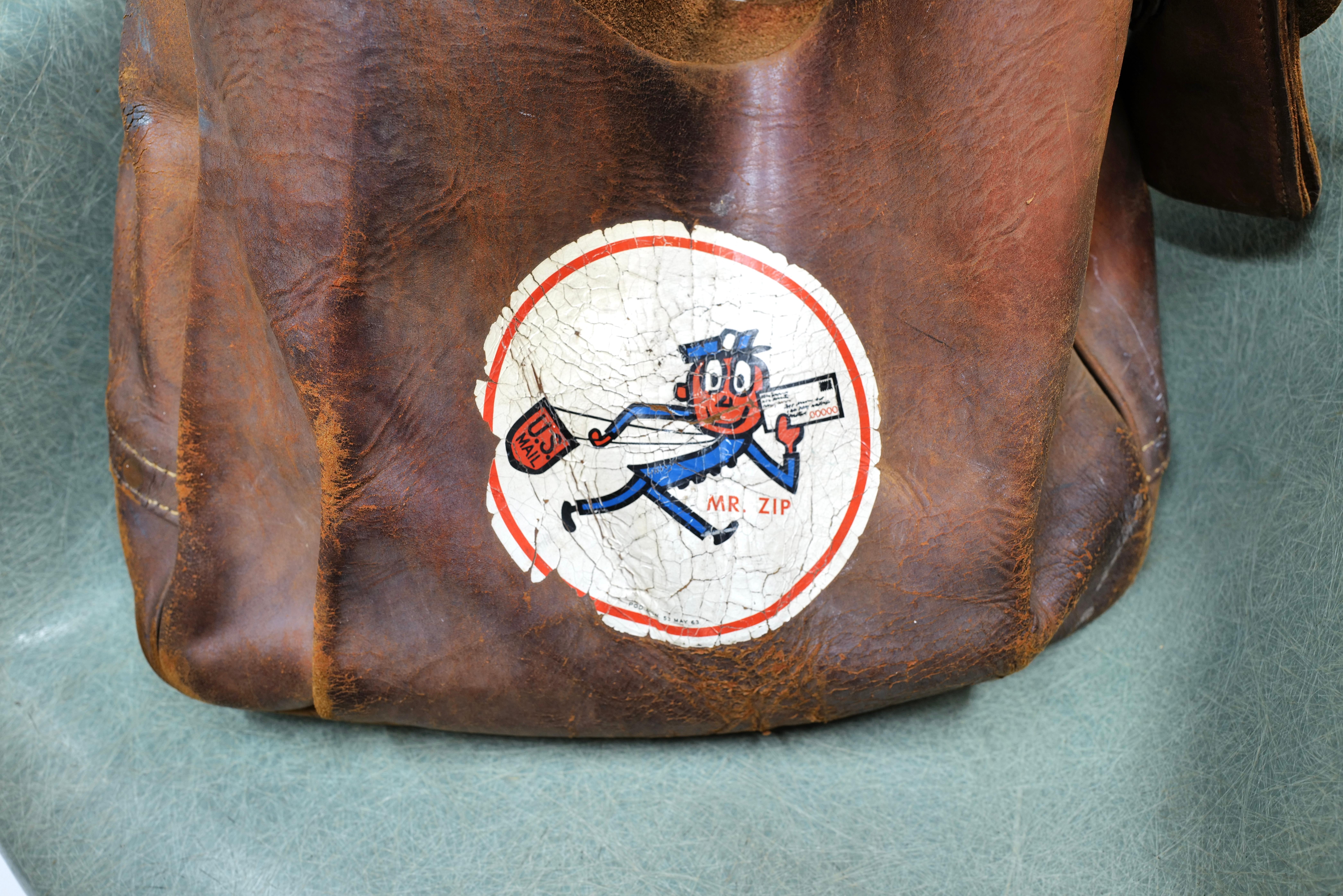 Behold, the vintage 1964 Leather Mr. Zip Postal Mail Bag, a timeless relic of postal history. Crafted from supple leather, this bag exudes a sense of elegance and durability, reminiscent of a bygone era. Adorned with the iconic Mr. Zip logo, it