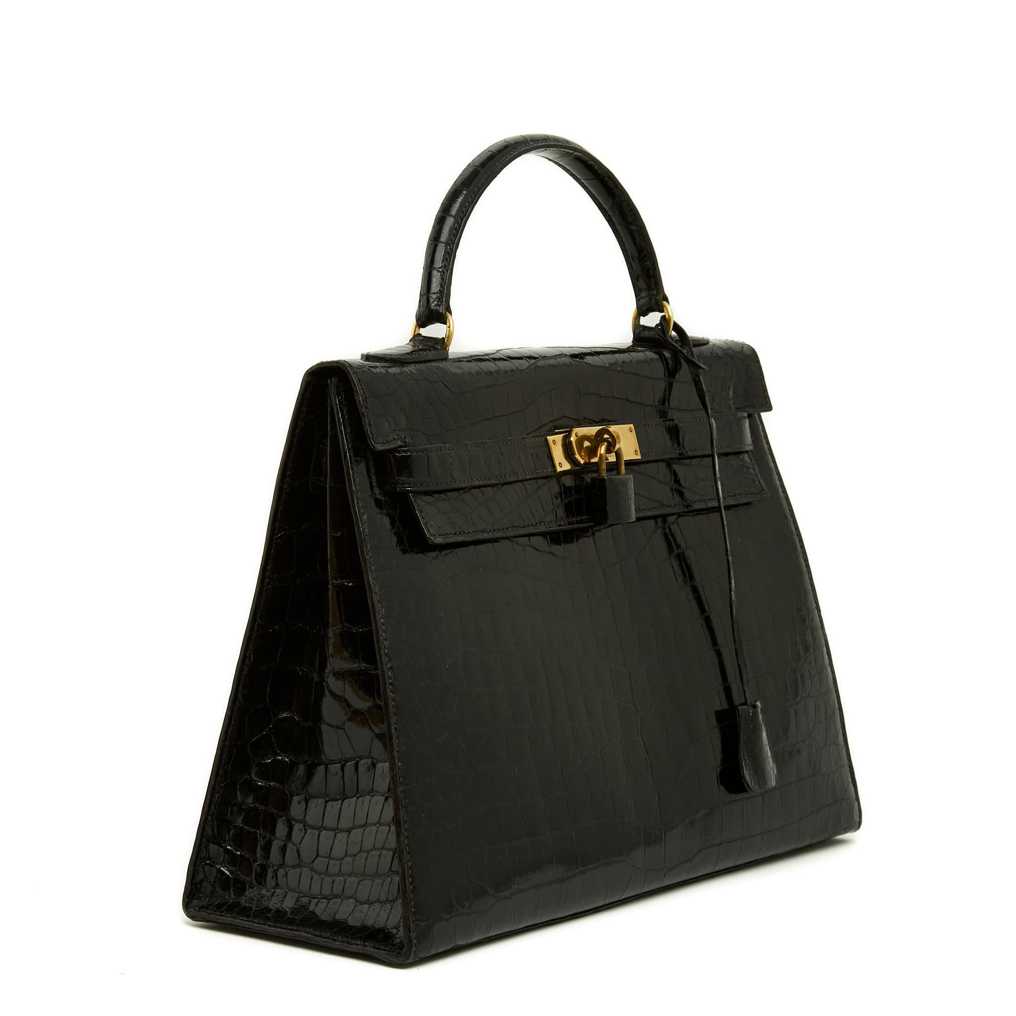 Bolso Hermès, modelo Kelly saddle, talla 32, de cocodrilo Porosus negro y metal dorado, hacia 1965, interior de piel negra con un bolsillo de parche en un lado y un bolsillo doble de parche en el otro, cremallera, timbre, llaves, candado forrado de