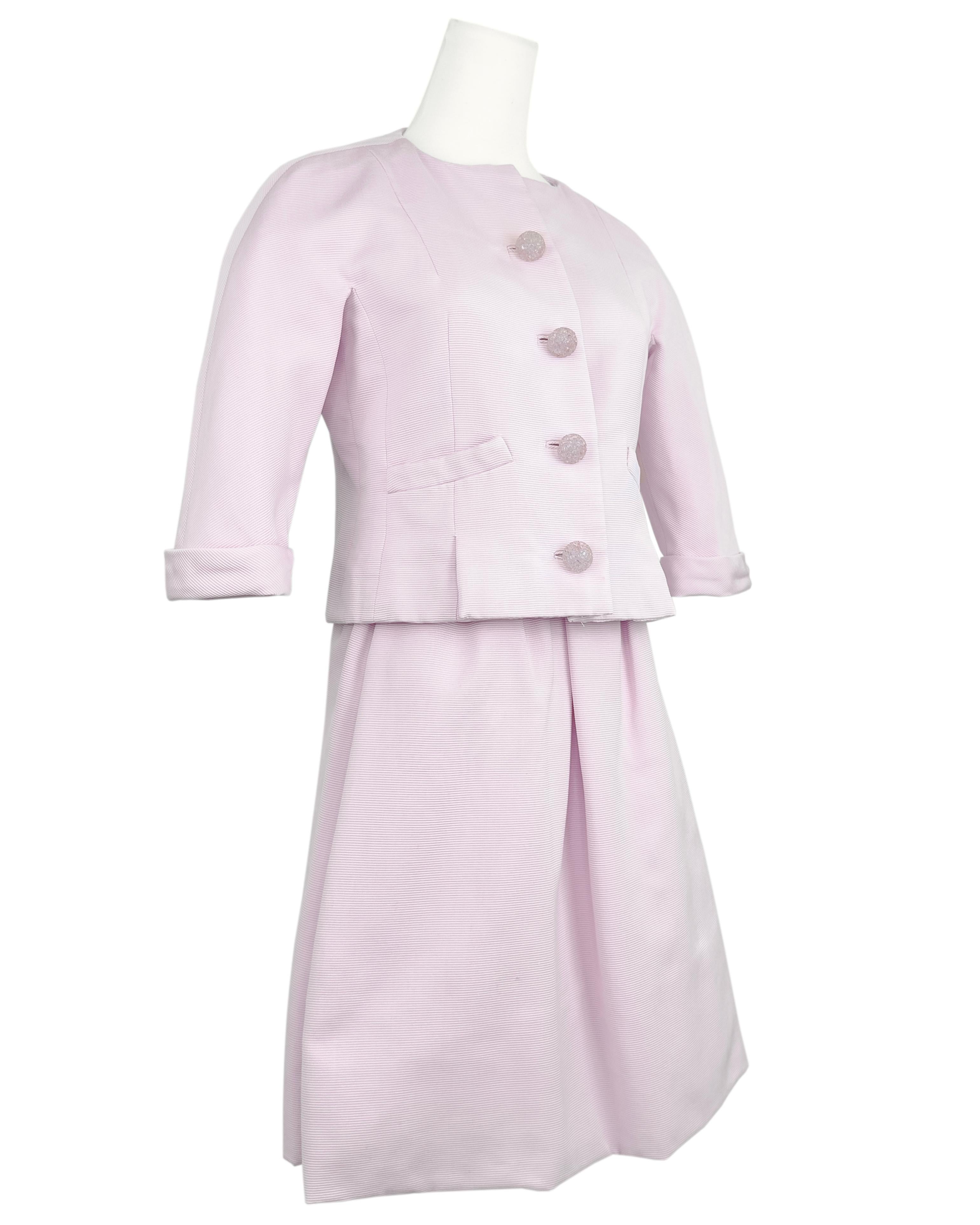 1966 Geoffrey Beene baby pink silk cordé fabric skirt suit. Cropped button front jacket with 3/4 length sleeves, small  pockets at the waist and darts that travel vertically down the front of the jacket ending in two front pleats. The pink plastic