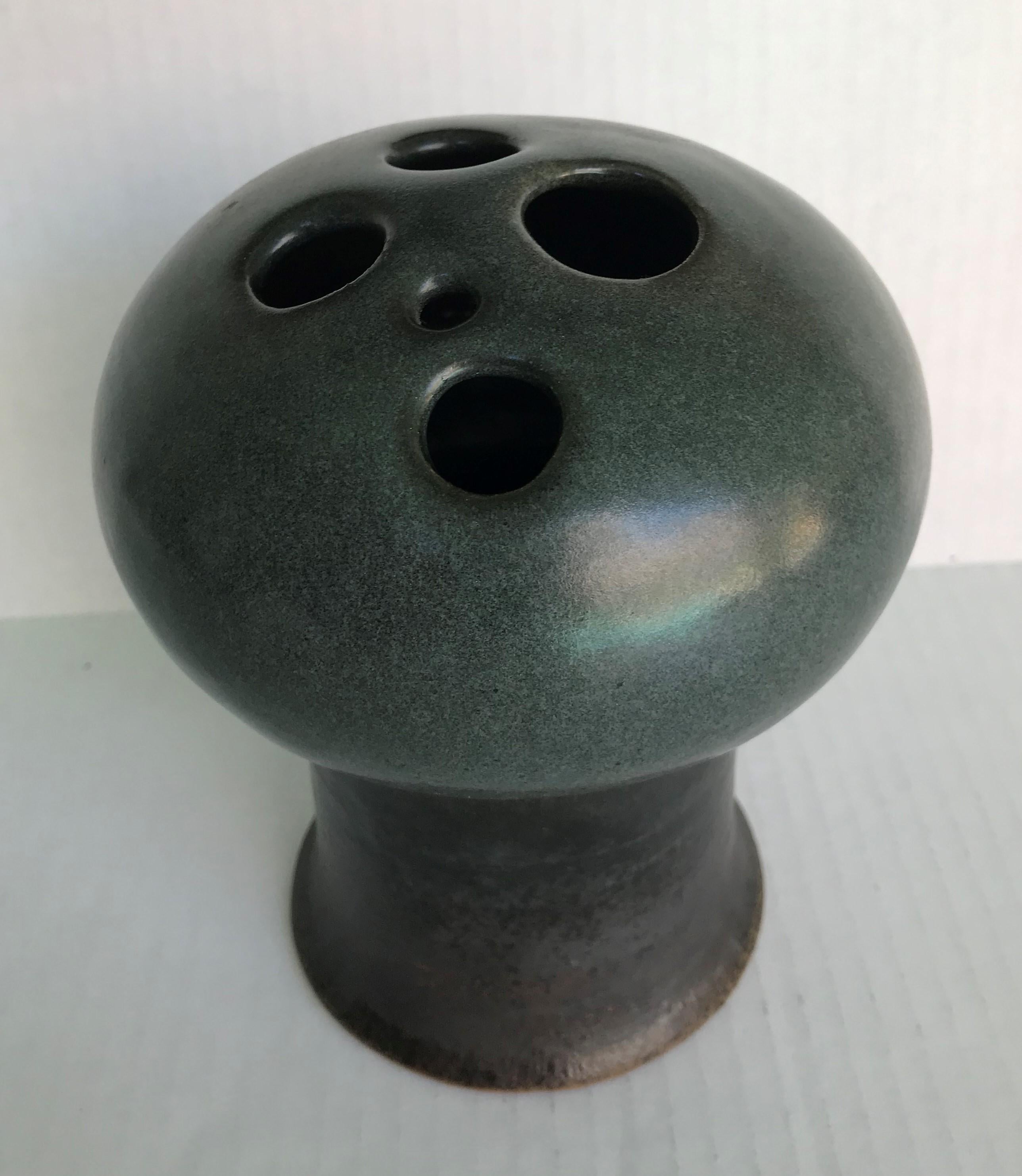 This glazed Victoria Littlejohn vase is signed and dated 1966. With a dark blue green gunmetal glaze, it is a stylized mushroom shape and has five circular holes in the top to receive flowers. A Weed Pot and a sign of the times it was made, a very
