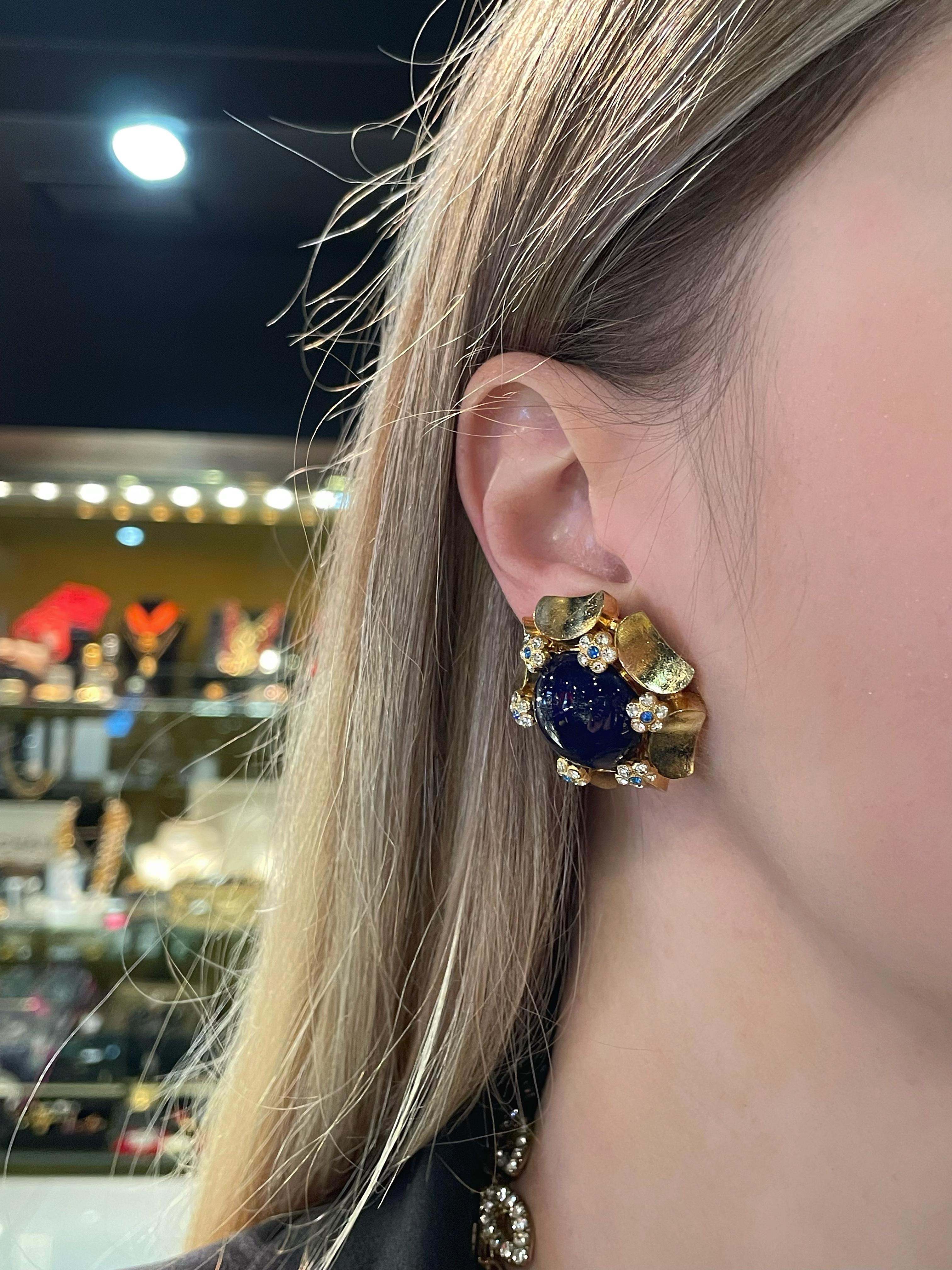 Es handelt sich um ein Paar Vintage-Ohrringe, die 1967 von Christian Dior entworfen wurden. Das Stück ist aus goldfarbenem, unedlem Metall gefertigt. Er ist mit violettblauen Gripoix-Glascabochons und glänzenden Kristallen besetzt. 

Gezeichnet: