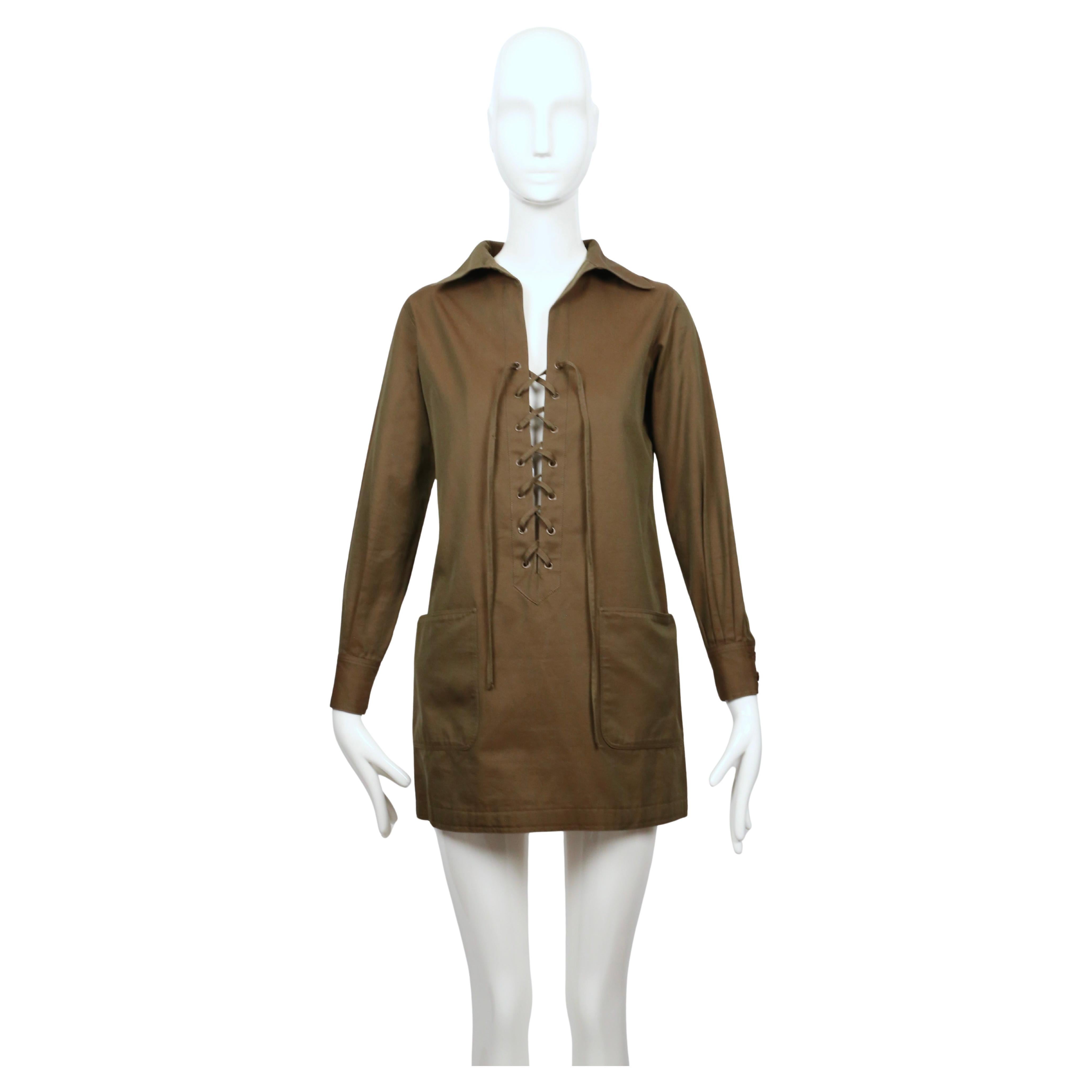 Túnica de safari extremadamente rara de Saint Laurent que data de 1968. De algodón pulido verde caqui oscuro con ligeras irisaciones. Tiene un cuello afilado y sobredimensionado y una parte delantera con cordones profundos y ojales metálicos que le