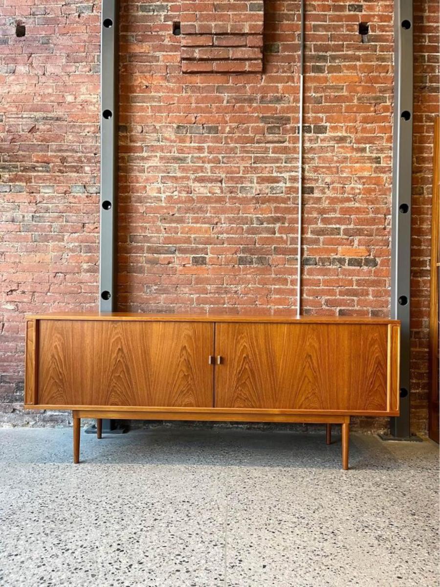 We are excited to offer this Peter Løvig Nielsen 1968 Teak Credenza. Crafted with meticulous attention to detail, this mid-century piece embodies the epitome of Danish design excellence. While the tambour doors that effortlessly glide open to reveal
