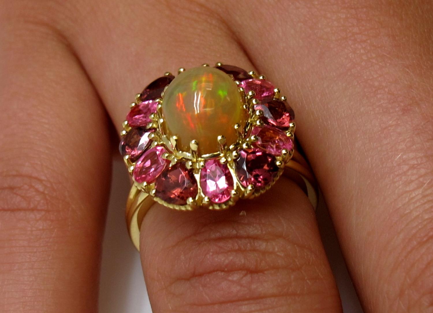 A fiery golden opal, luscious pink spinels and rich rhodolite garnets - an original combination for a truly original person! This handmade, 18k yellow gold ring features a colorful opal  complemented by oval shaped bright pink spinels and pear