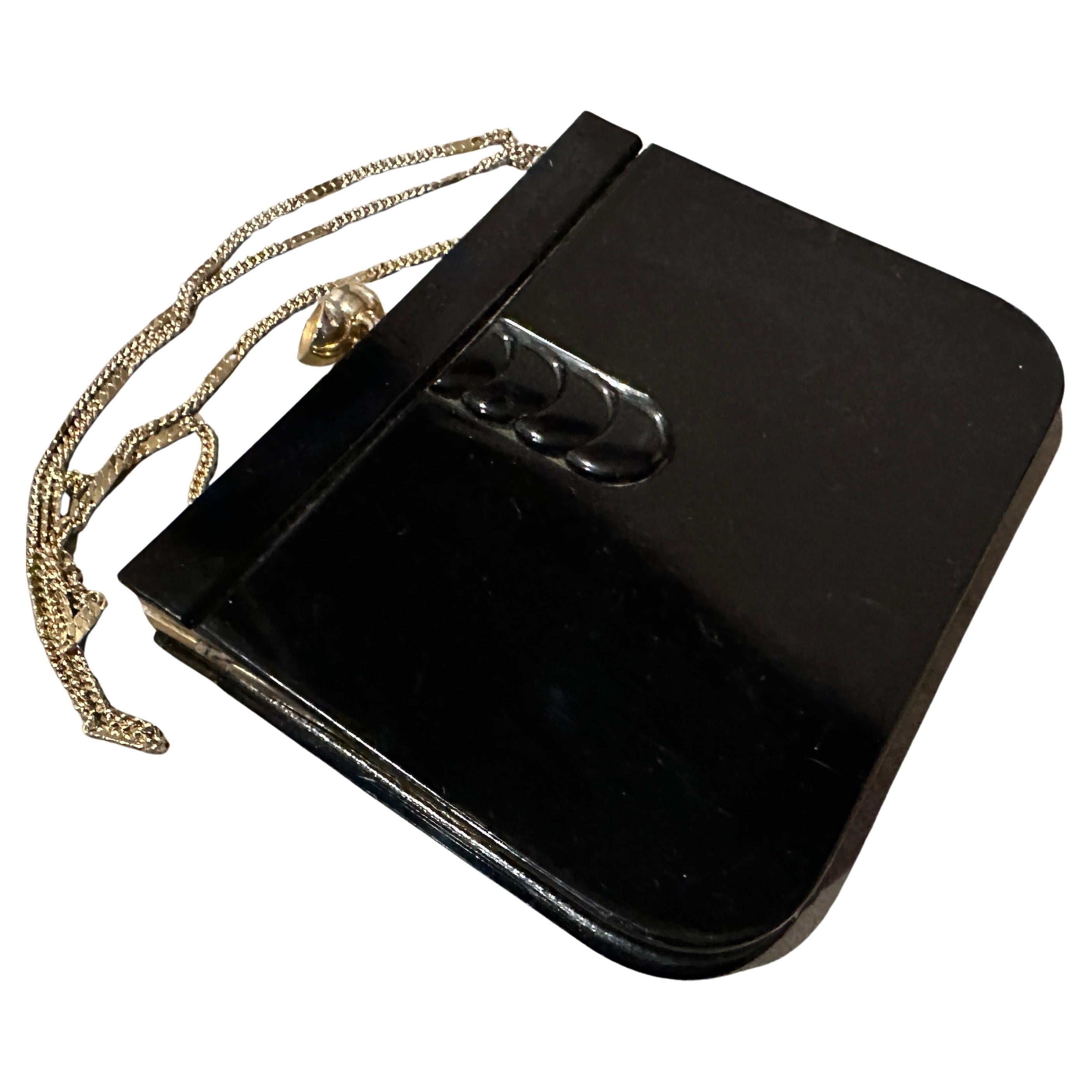 Questa borsa a tracolla vintage degli anni '70, unica nel suo genere, è un esempio lampante di stile Art Deco revival. Presenta un corpo elegante e strutturato, realizzato in bachelite nera o in un materiale simile, che gli conferisce una finitura