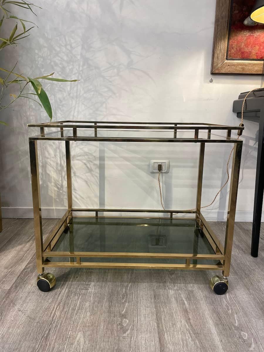 Chariot de bar à deux plateaux avec cadre en laiton et verre fumé. 
Le cadre en laiton est en tube carré, les vitres sont en position debout et les roues sont d'origine. 

Dimensions : 70 cm x 48 cm x H 60,6 cm.

Le prix INCLUT le coût de