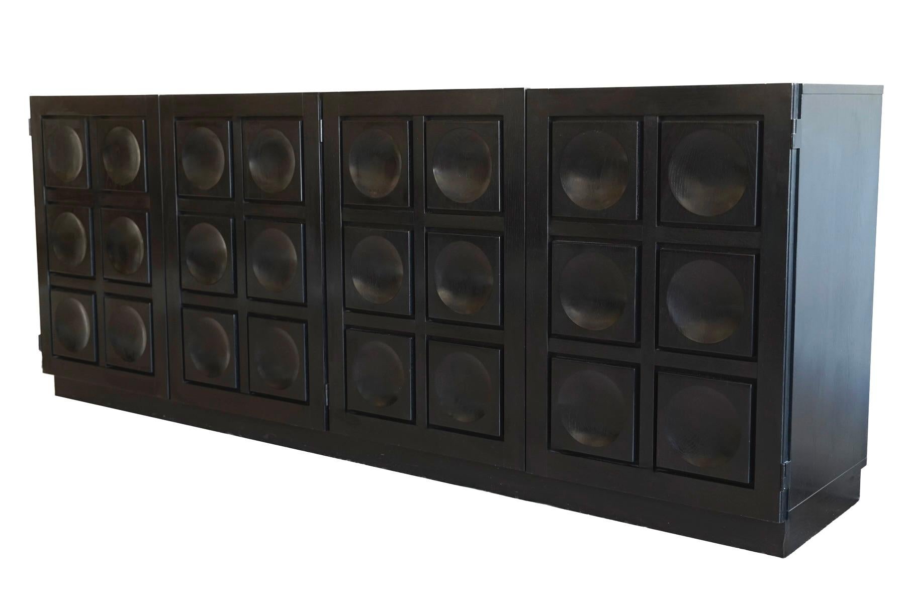 Il se compose d'une grande base rectangulaire s'ouvrant sur 4 portes bien ajustées qui, une fois fermées, présentent un motif géométrique de carrés et de cercles concaves. Les poignées sont dissimulées dans les bords supérieurs et intérieurs des