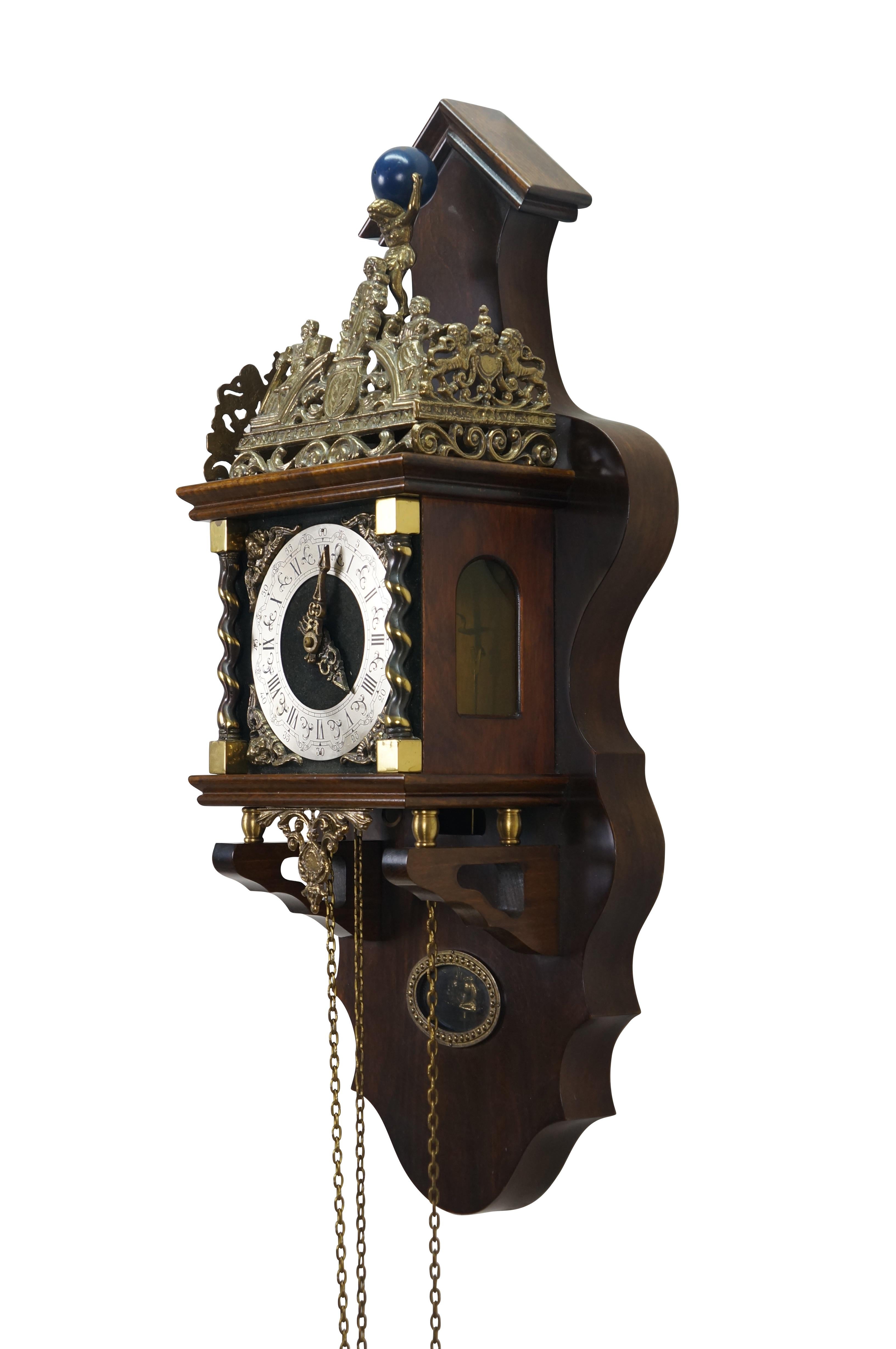 Vintage 1970's Warmink / WUBA Zaanse wall clock. Dark wood case with scalloped sides and peaked pediment. Metallic face with black Roman numerals and brass filigree hands, flanked with winged cherubs at the corners and a pair of twisted brass