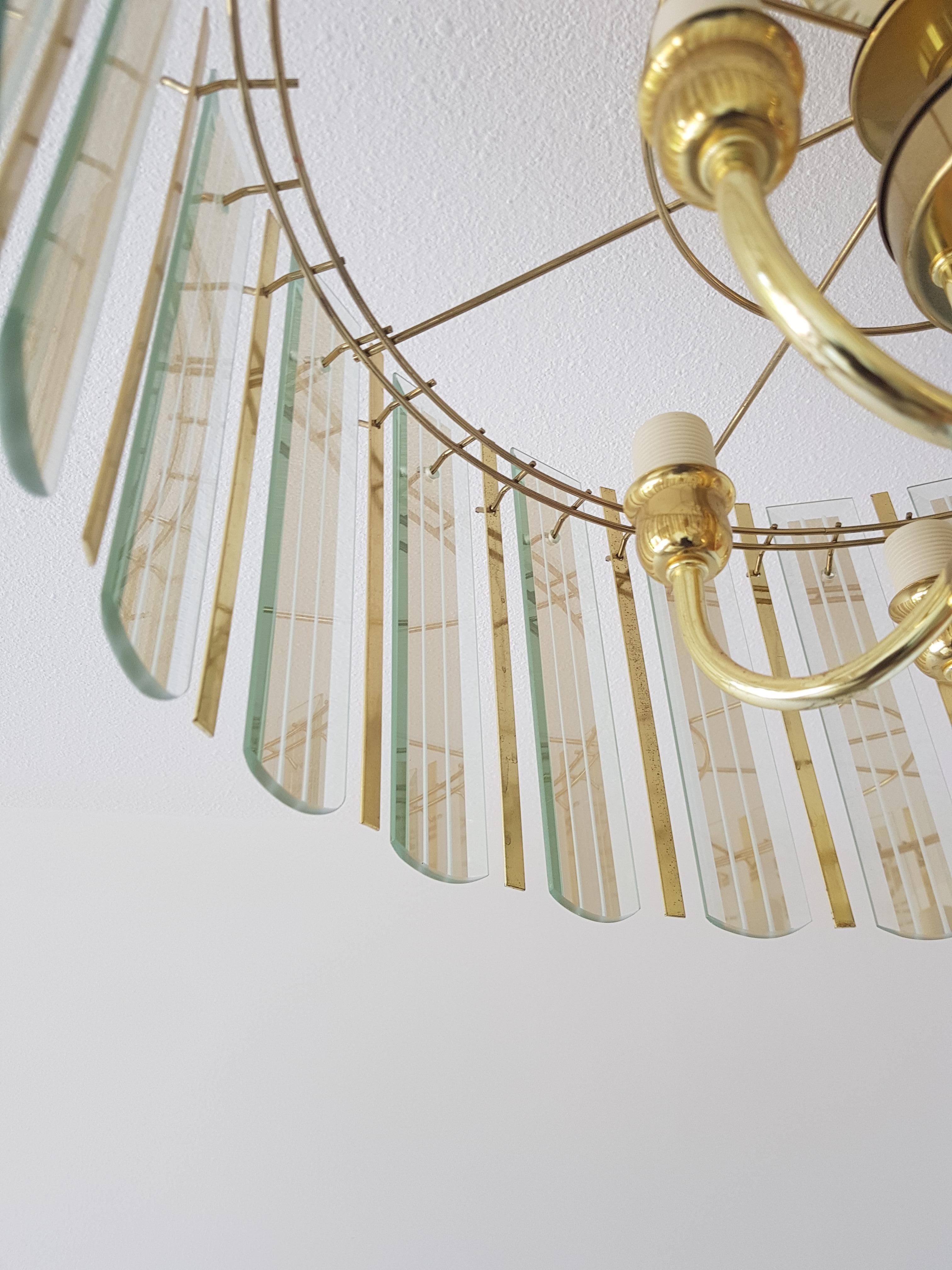 A unique chandelier from the seventies, glass with brass pieces between it and the rectangular glass with mirror finish, this chandelier could be in a James Bond movie.
It has six lamps on top and one big in the middle.
Length can be adjusted by
