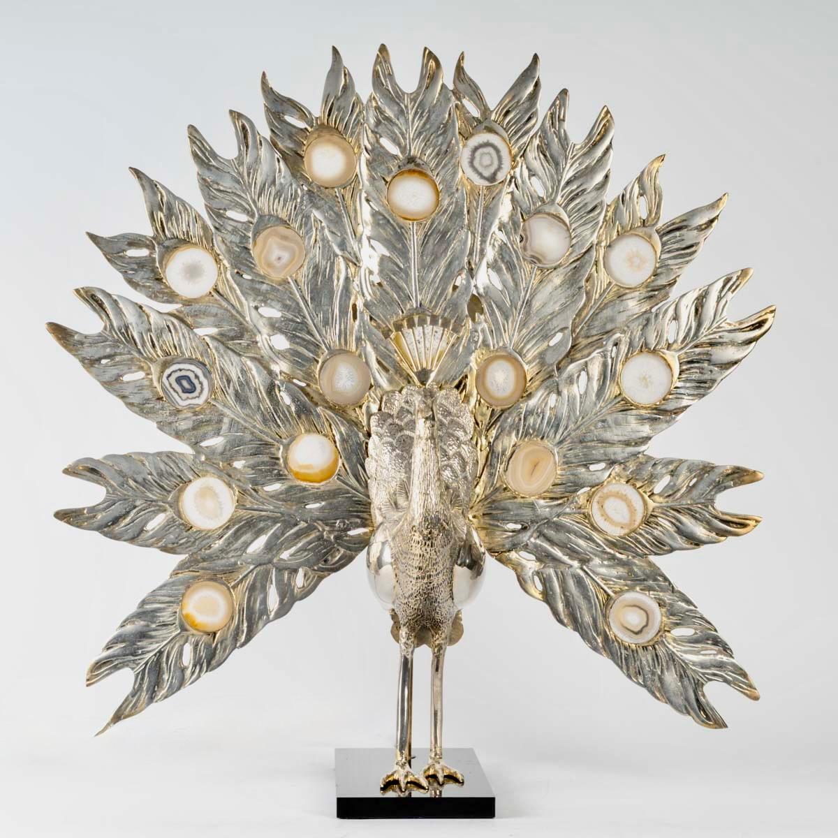 Gran Lámpara Pavo Real haciendo la rueda en bronce con pátina dorada y plateada e inclusión de discos de piedra ágata dura.
Compuesto por una base rectangular de piedra negra sobre la que descansa un gran Pavo Real haciendo la rueda.
La rueda de