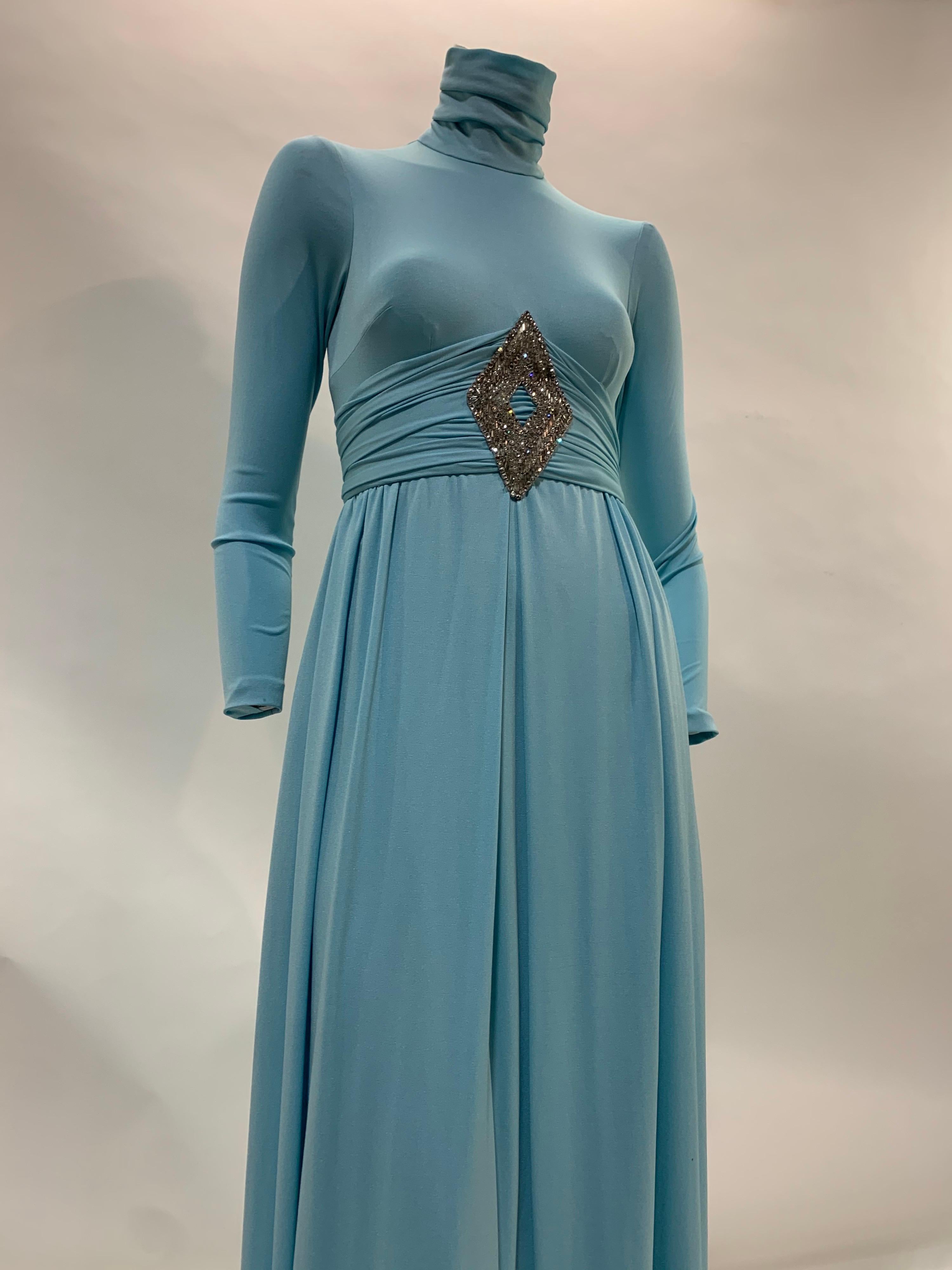 Early 1970s Lillie Rubin aquamarine knit synthetic maxi dress or gown with high gathered neck, long tapered sleeves, sleek bodice and pleated skirt. Peaked cummerbund style gathered waist with beautiful rhinestone and bugle bead embellished center