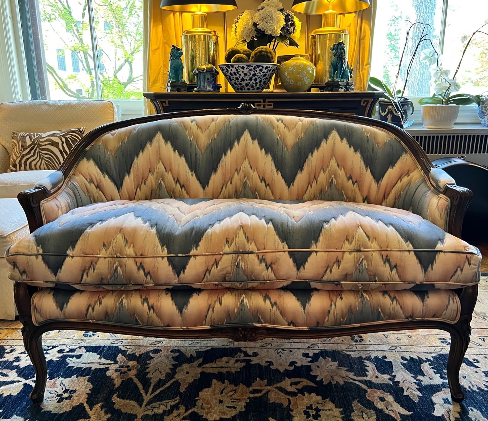 A vintage Louis XV style curved settee with carved wood details. The sofa was upholstered in 1970 in flamestitch cotton fabric in a blue and peach colorway. The fabric has been hand quilted following the contours of the flamestitch pattern. The seat