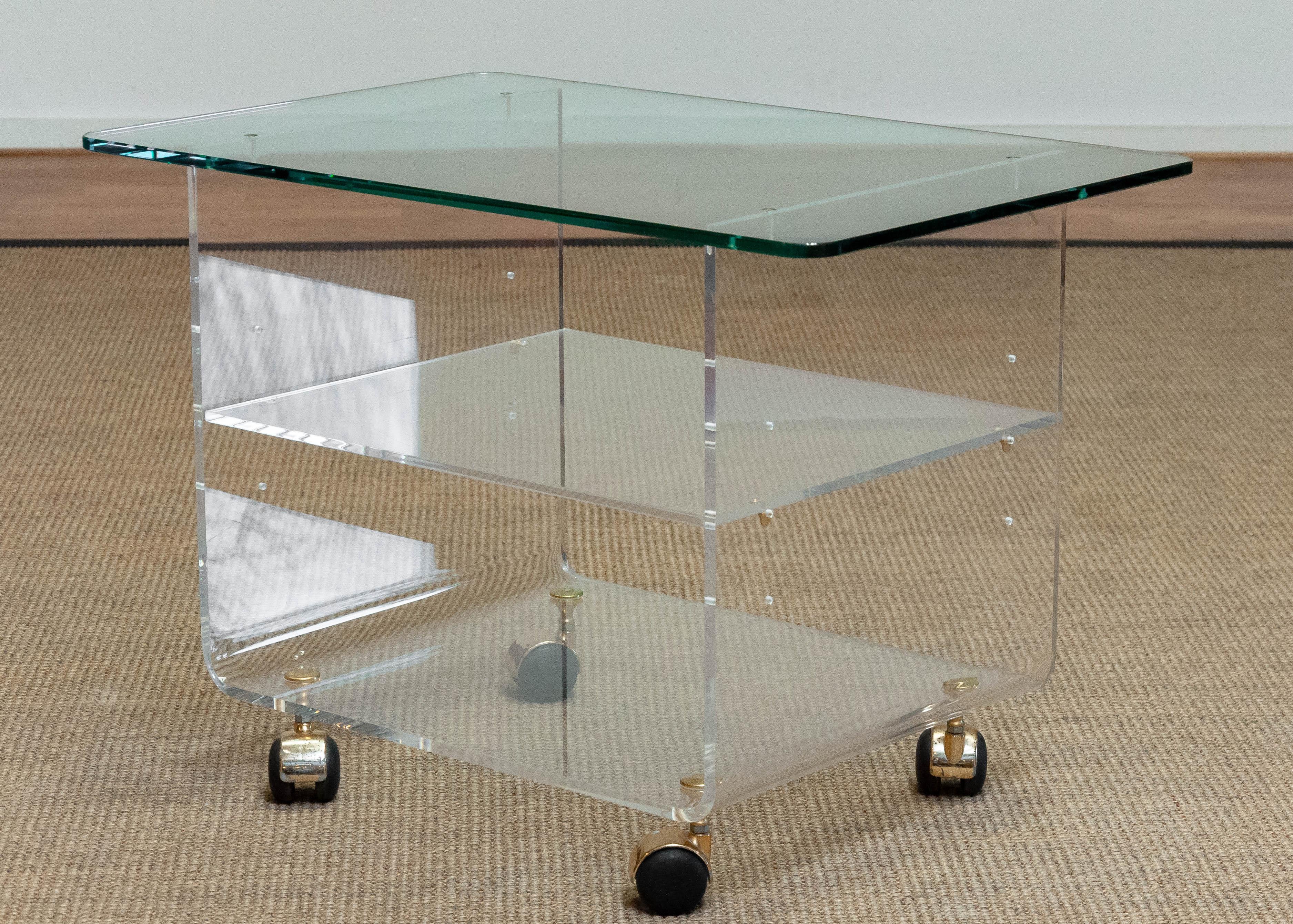 Moderen Lucite side table with glass top designed by the French Designer David Lange.
This Lucite side table has one shelf what is adjustable in three different positions.
Resting on four casters (brass colored).
 