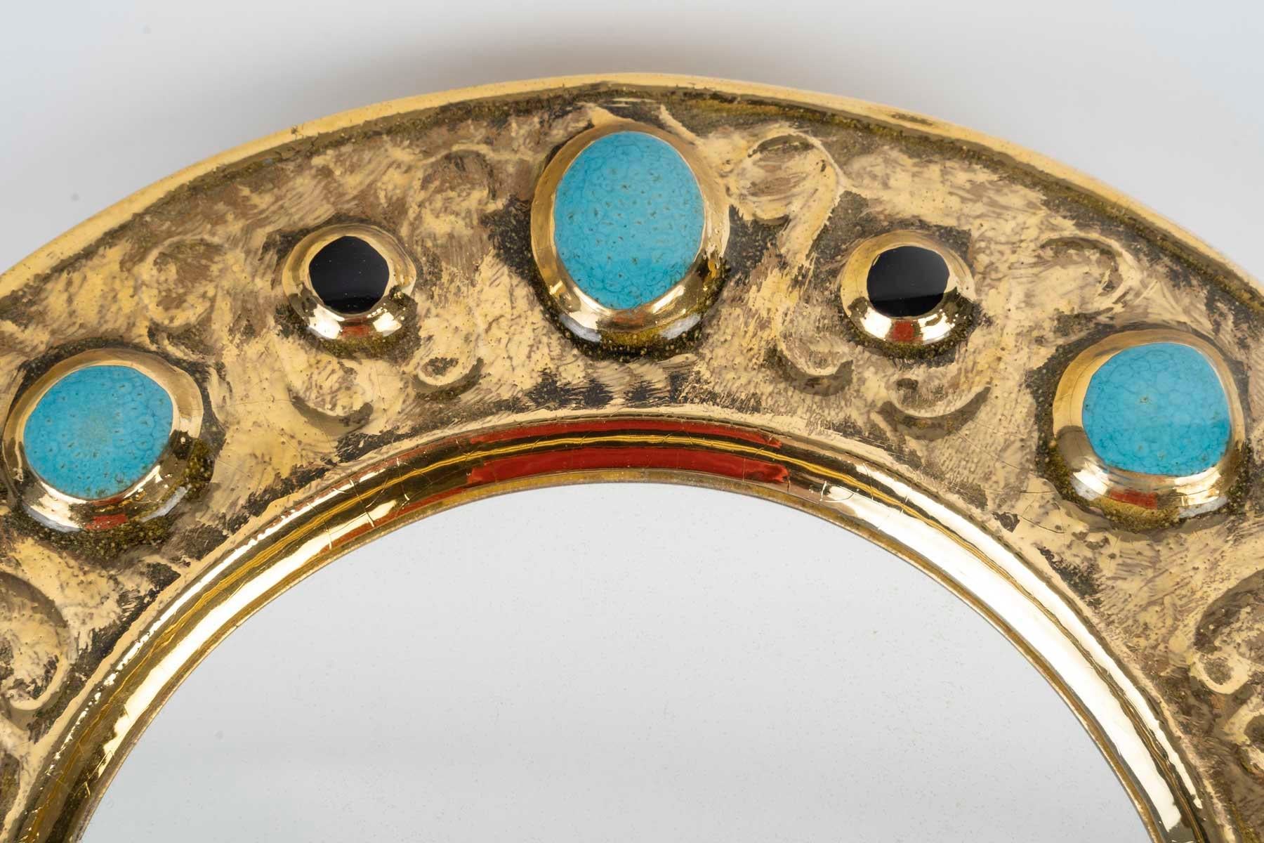 
Miroir François Lembo, céramique, bijoux, or, vert émeraude, noir signé. Petit miroir circulaire, émaillé d'or, à décor de bijoux incrustés. Signé F. Lembo avec signature incisée au dos. 

Originaire de Vallauris, François Lembo a commencé sa