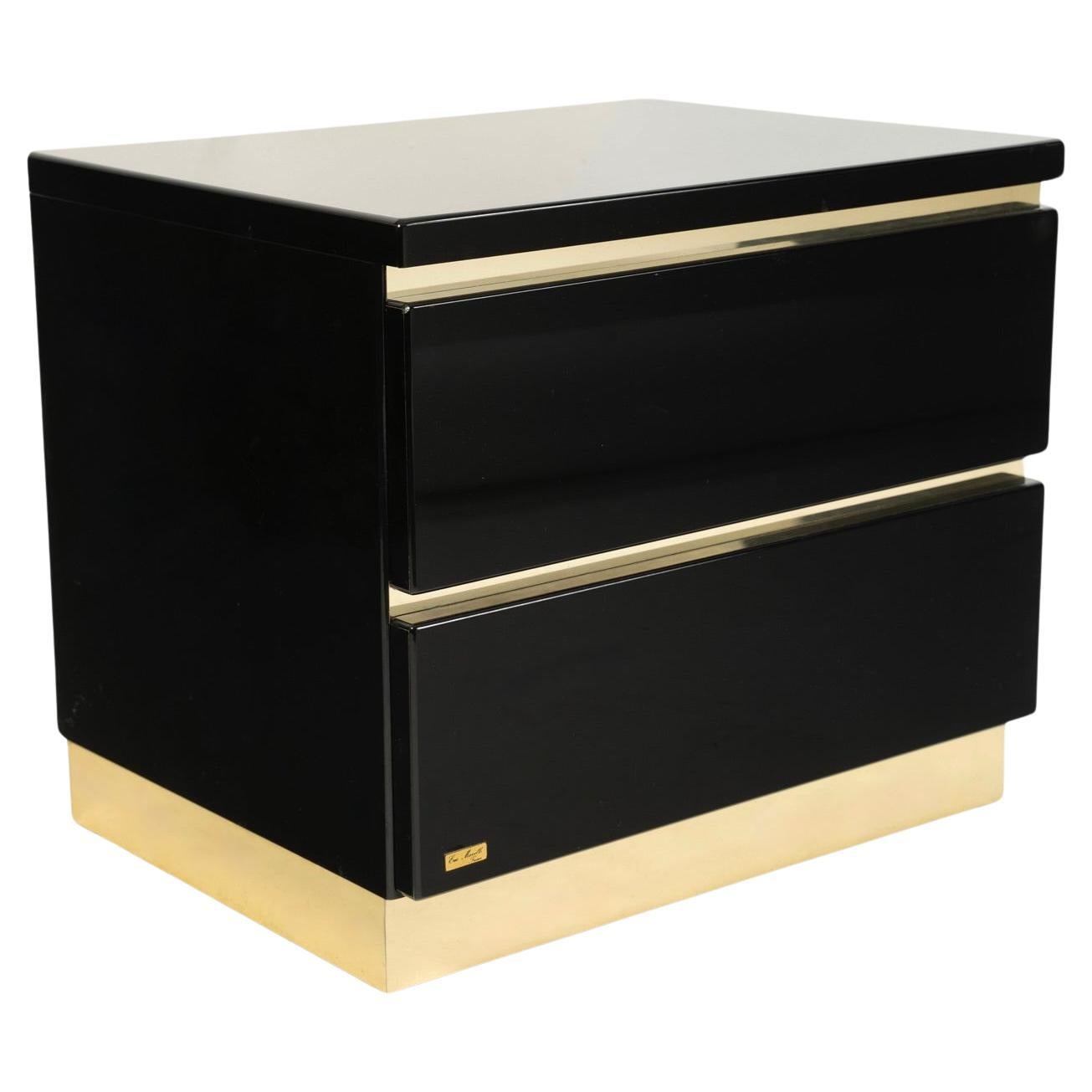 Composed of a rectangular cube in black acrylic-lacquered wood, highlighted at the base by a wide band of gilded brass.
It features two drawers opening from the front, highlighted at the top of each drawer by a gilded brass band.
The signature plate