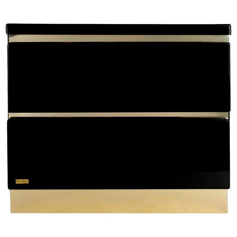 Composed of a rectangular cube in black acrylic-lacquered wood, highlighted at the base by a wide band of gilded brass.
It features two drawers opening from the front, highlighted at the top of each drawer by a gilded brass band.
The signature plate