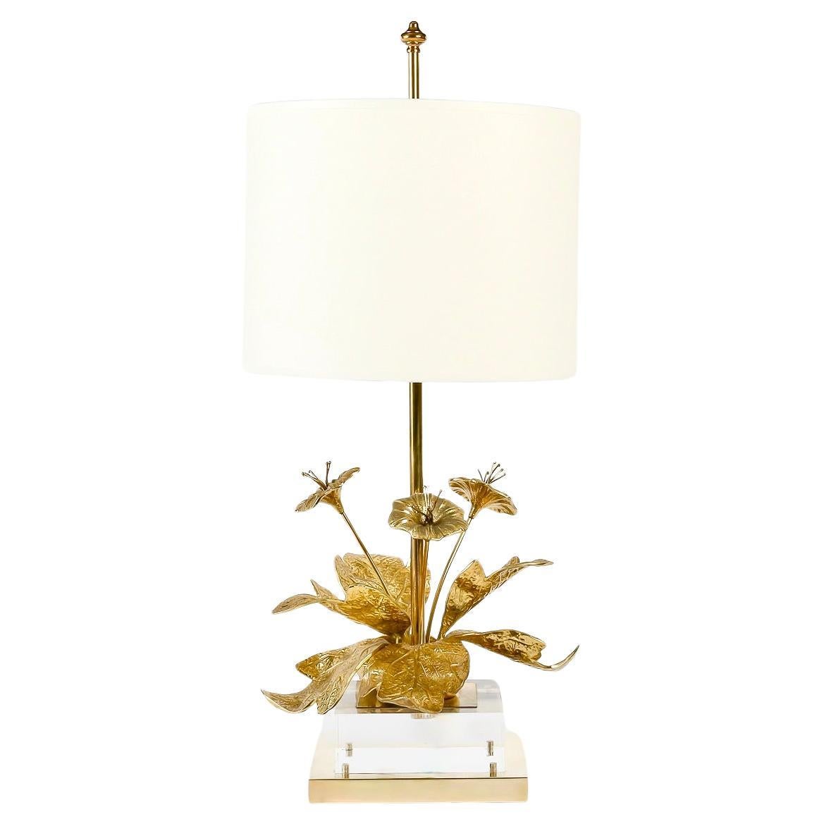 Comprising a square gilded-brass base on which rests a Plexiglas cube, above which is a smaller gilded-brass plate, the lamp is decorated just above with a pretty bouquet of gilded-bronze flowers and foliage scattered around the lamp's perimeter.
In