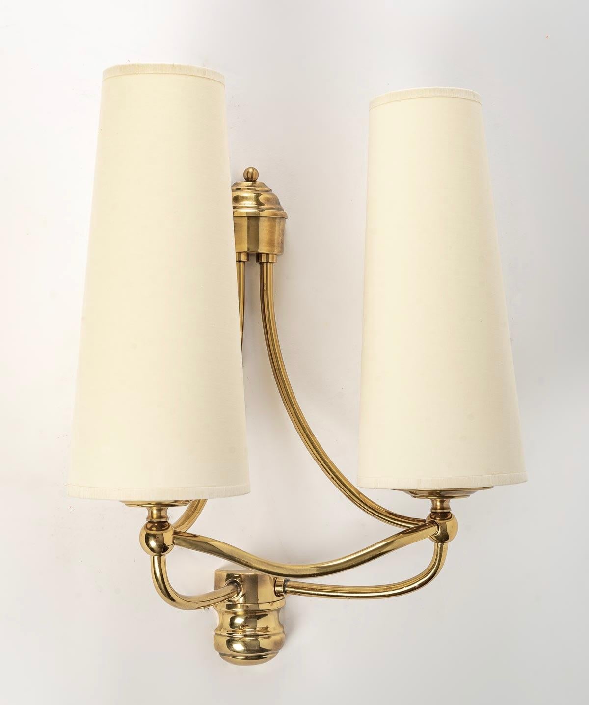 1970 pair of gilt brass sconces by Maison Roche

Each wall lamp is composed of two light arms distributed on each side of the wall lamp in gilded brass and underlined by nicely curved gilded brass rods.
Two handmade shades in off-white cotton cover