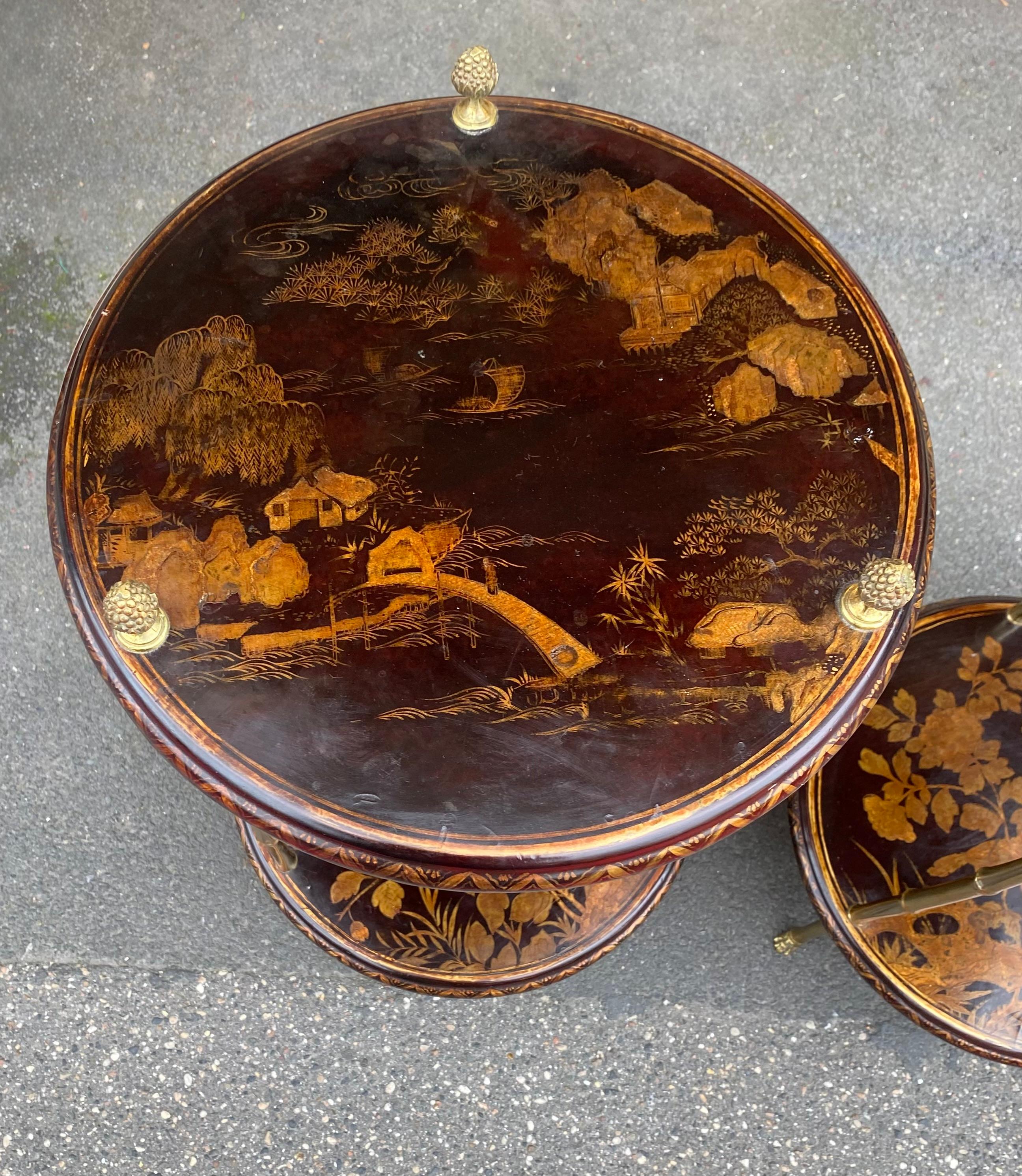 Coppia di tavoli con piedistallo in bronzo dorato con decorazioni in bambù e piani rotondi in legno laccato cinese ornati da uccelli, figure, paesaggi montani e un fiume con un ponte. I montanti terminano con delle pigne e i piedi sono a forma di