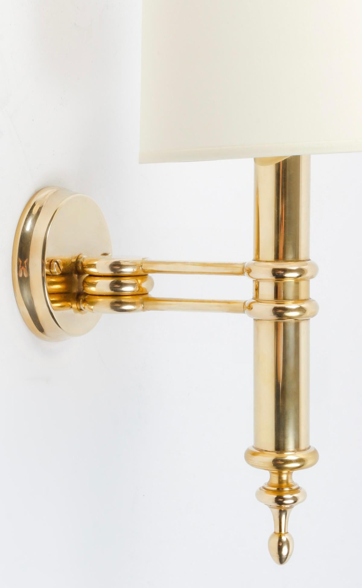 Composed of a gilded bronze wall bracket on which rests an arm composed of two rods supporting the cylindrical-shaped light arm embellished on the lower part with an oval point.
On the upper part, an off-white, trapezoid-shaped cotton lampshade