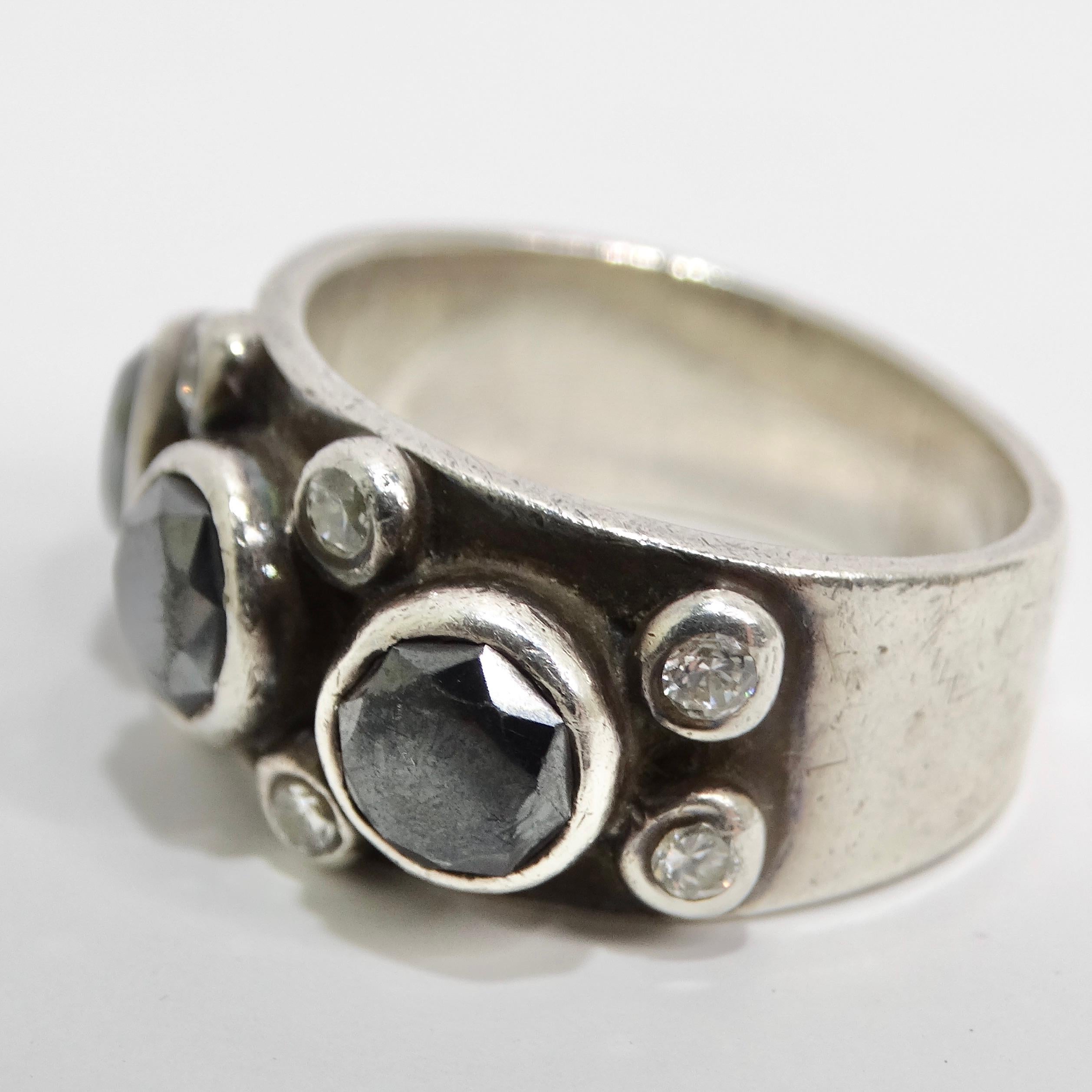 Versetzen Sie sich in die schillernde Ära der 1970er Jahre mit unserem exquisiten Ring aus reinem Silber mit synthetischem Diamant. Dieser Ring ist aus einem dicken Silberband gefertigt und mit drei auffälligen synthetischen Diamanten in Schwarz und