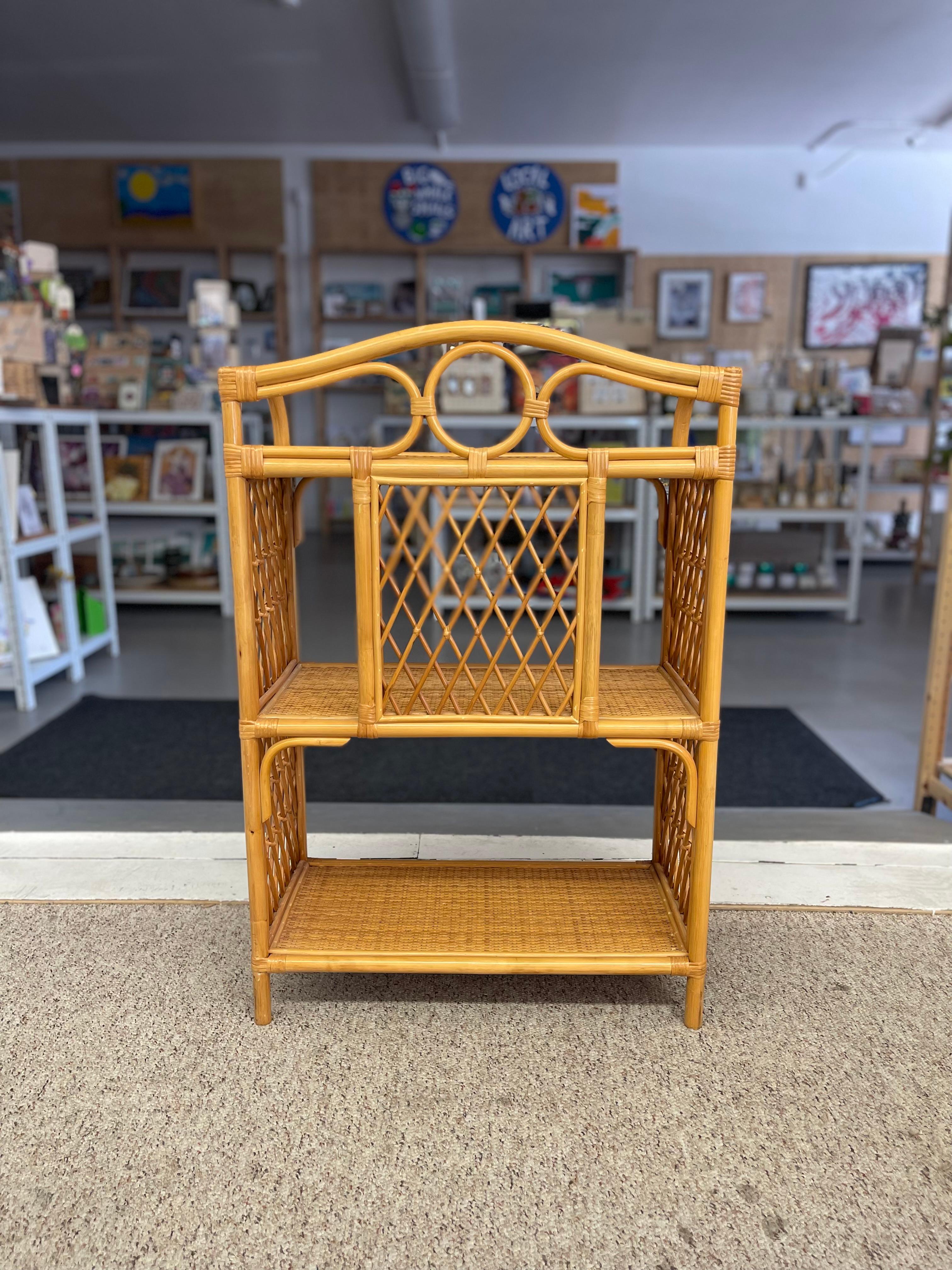 Esta estantería etagere vintage de tres niveles, fabricada probablemente en la década de 1970, presenta una llamativa mezcla de ratán y mimbre tejido con un detallado trabajo artesanal. El armazón de ratán natural está curvado con vapor en suaves