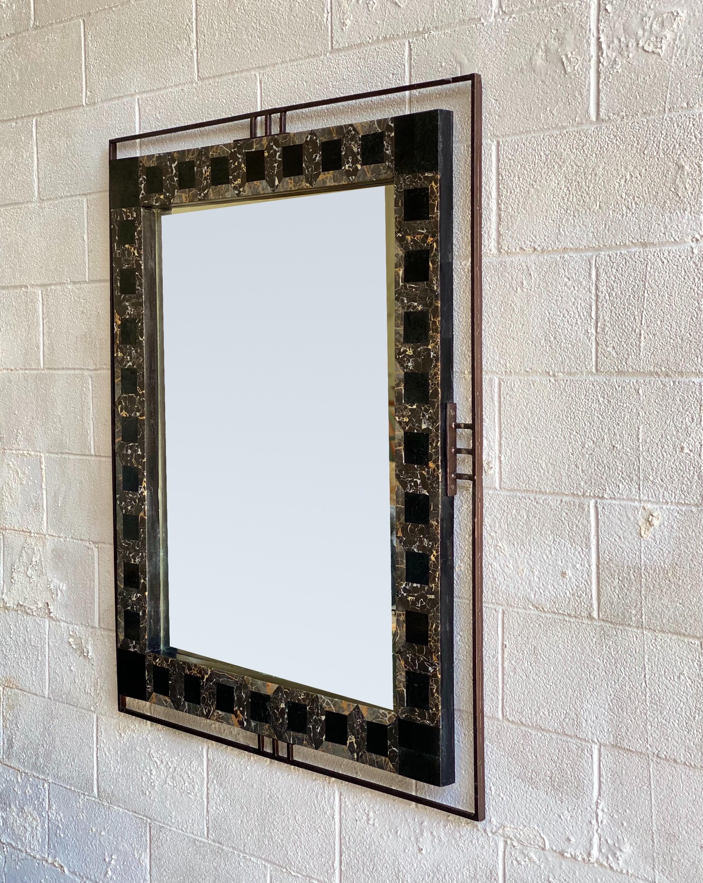 We are very pleased to offer a sculptural wall mirror, circa the 1970s. A rectangular tessellated marble highlights the material's organic texture, while a slim iron frame gives it an industrial character in sculptural style. Natural black and brown