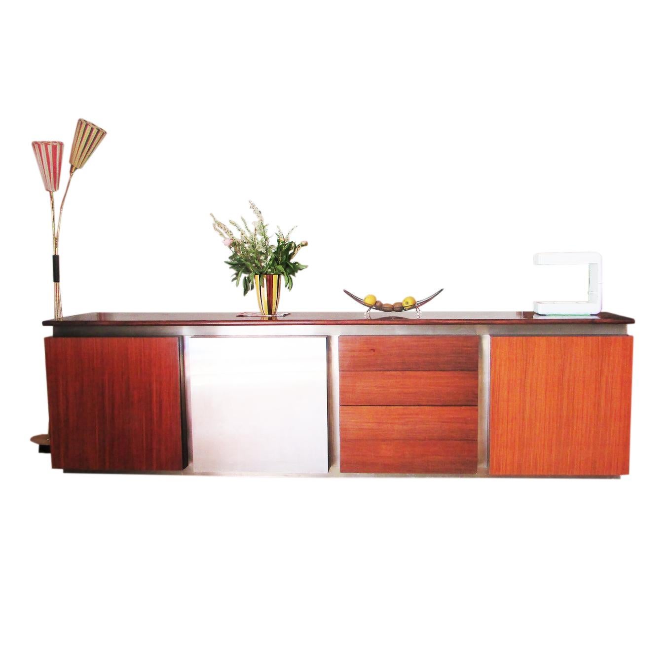 Stainless steel and mahogani sideboard designed in 1972 by Giotto Stoppino for Acerbis.
Four elements that can be combined at will, three with a wooden door and the forth covered with metal.
The metal cabinet door slide to open and reveal a dry