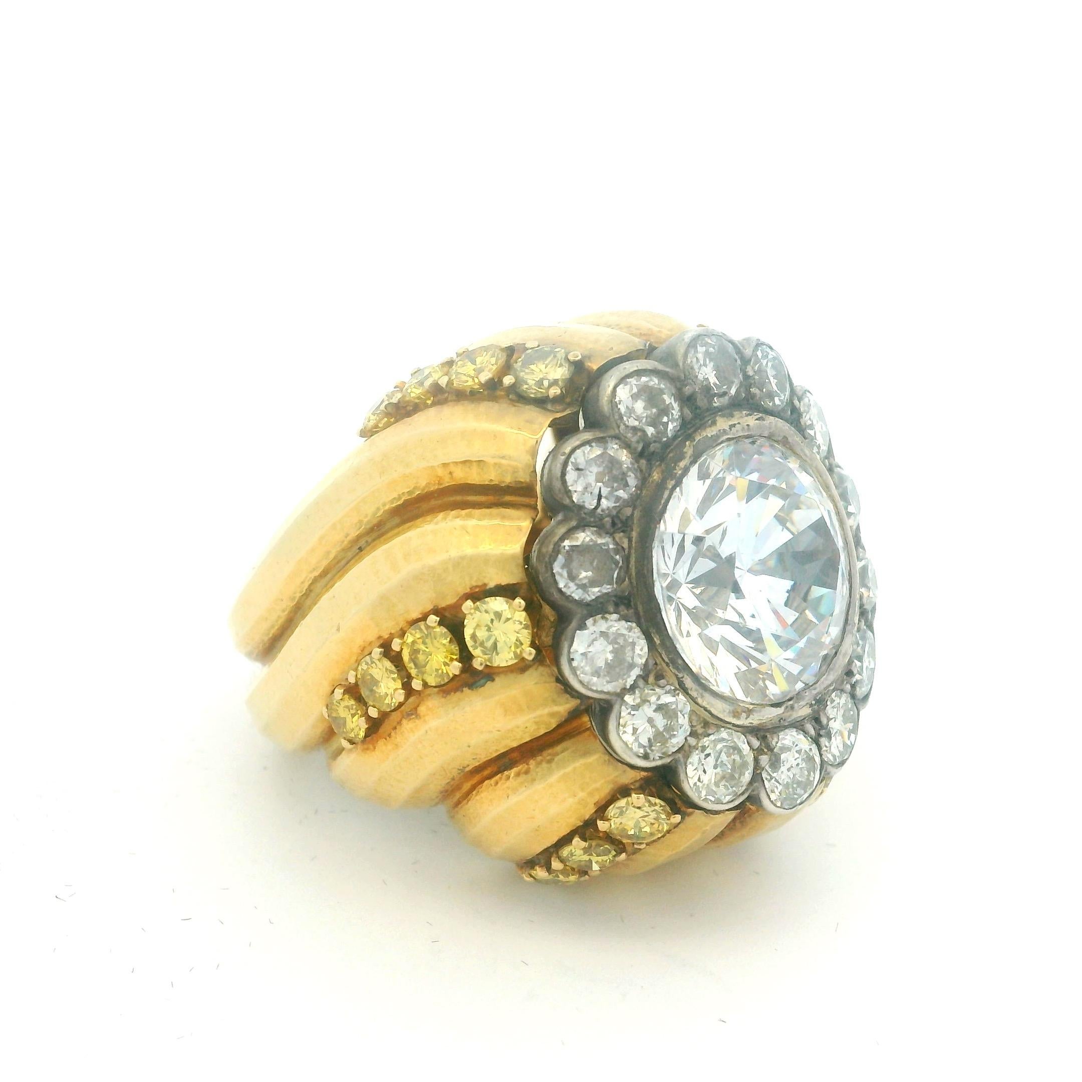 Dagli anni '70, questo anello bombe in oro 18 carati unisce una forma forte, un peso consistente e un'impressionante presenza di gemme. Il centro presenta uno zaffiro bianco da 10 carati incastonato in una cornice circolare di 14 diamanti bianchi