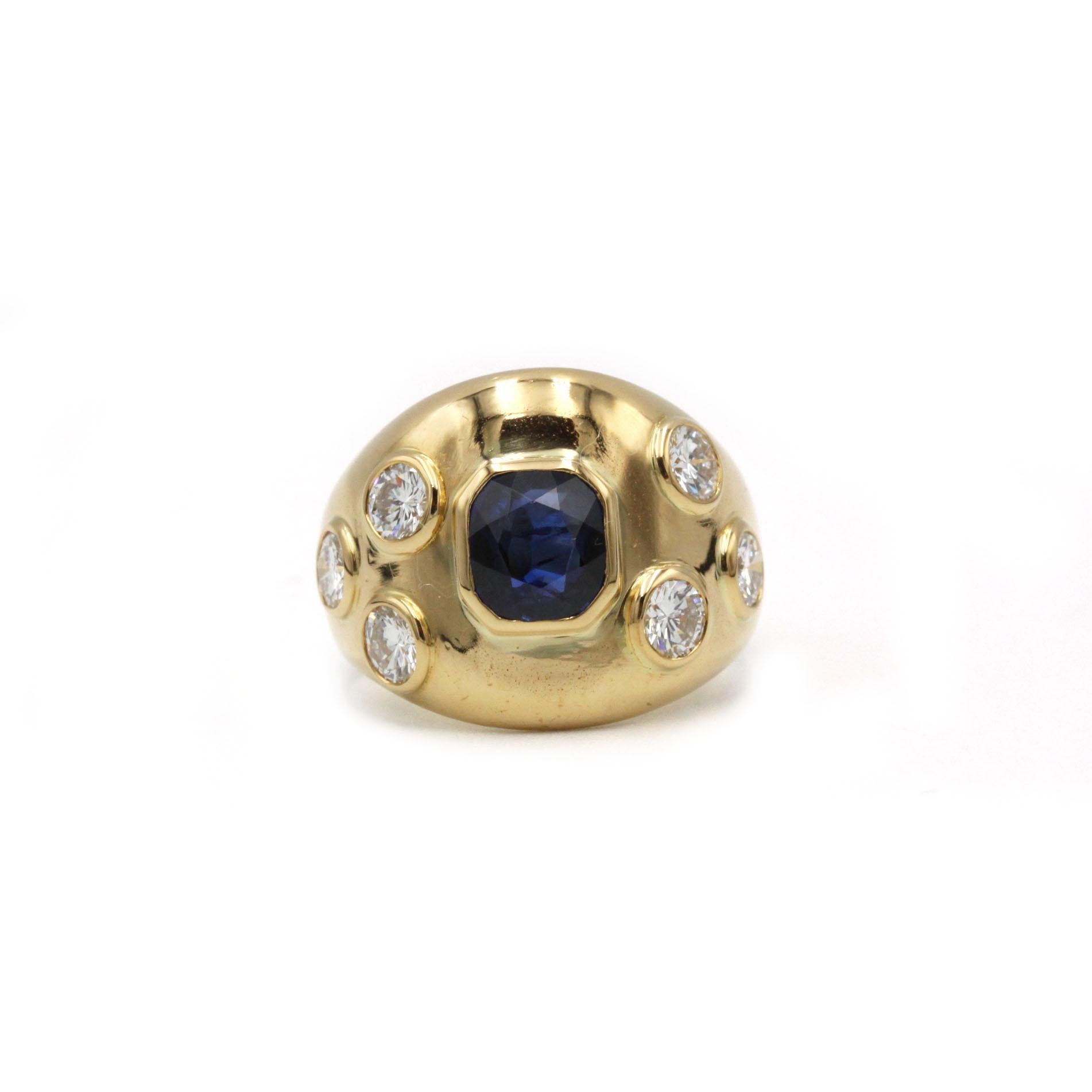 Anello con zaffiro e diamanti in oro giallo 18 carati degli anni '70 - un anello da cocktail audace e scultoreo con uno zaffiro sfaccettato riccamente saturo incastonato al centro e sei diamanti brillanti disposti sulle spalle a cupola. Lo zaffiro