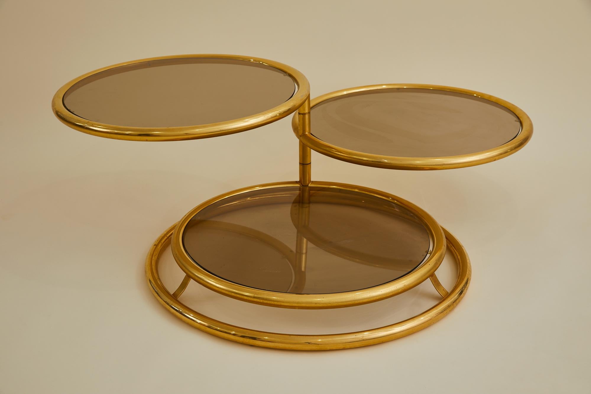 This Mid-Century circular table is made of brass plated tubular steel. It has 3 articulating tiers that swivel a full 360 degrees– each with a removable smoked glass top. This versatile piece is made in the style of DIA (Design Institute of America)