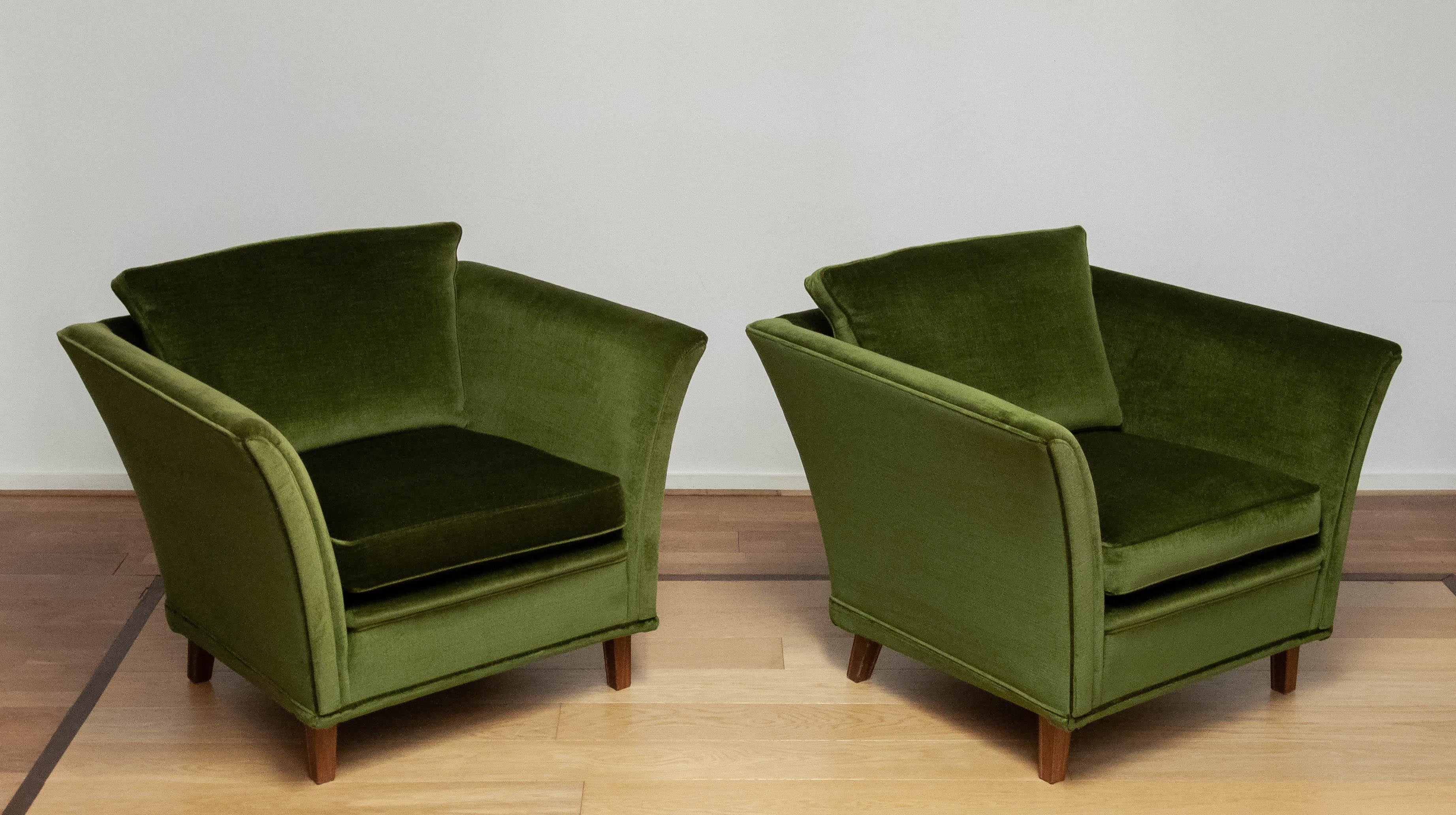 Un par de tumbonas suecas de los años 70, tapizadas en lujosa tela de terciopelo verde. Estos sillones presentan un diseño limpio y acogedor, con reposabrazos ligeramente acampanados, cojines de felpa para el asiento y el respaldo, y robustas patas