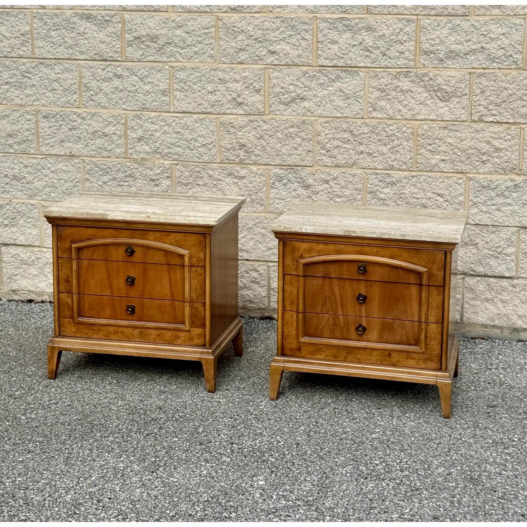 A pair of nightstands featuring three drawers elegantly accented with brass details and crafted from rich burled wood. Removable travertine tops. 



