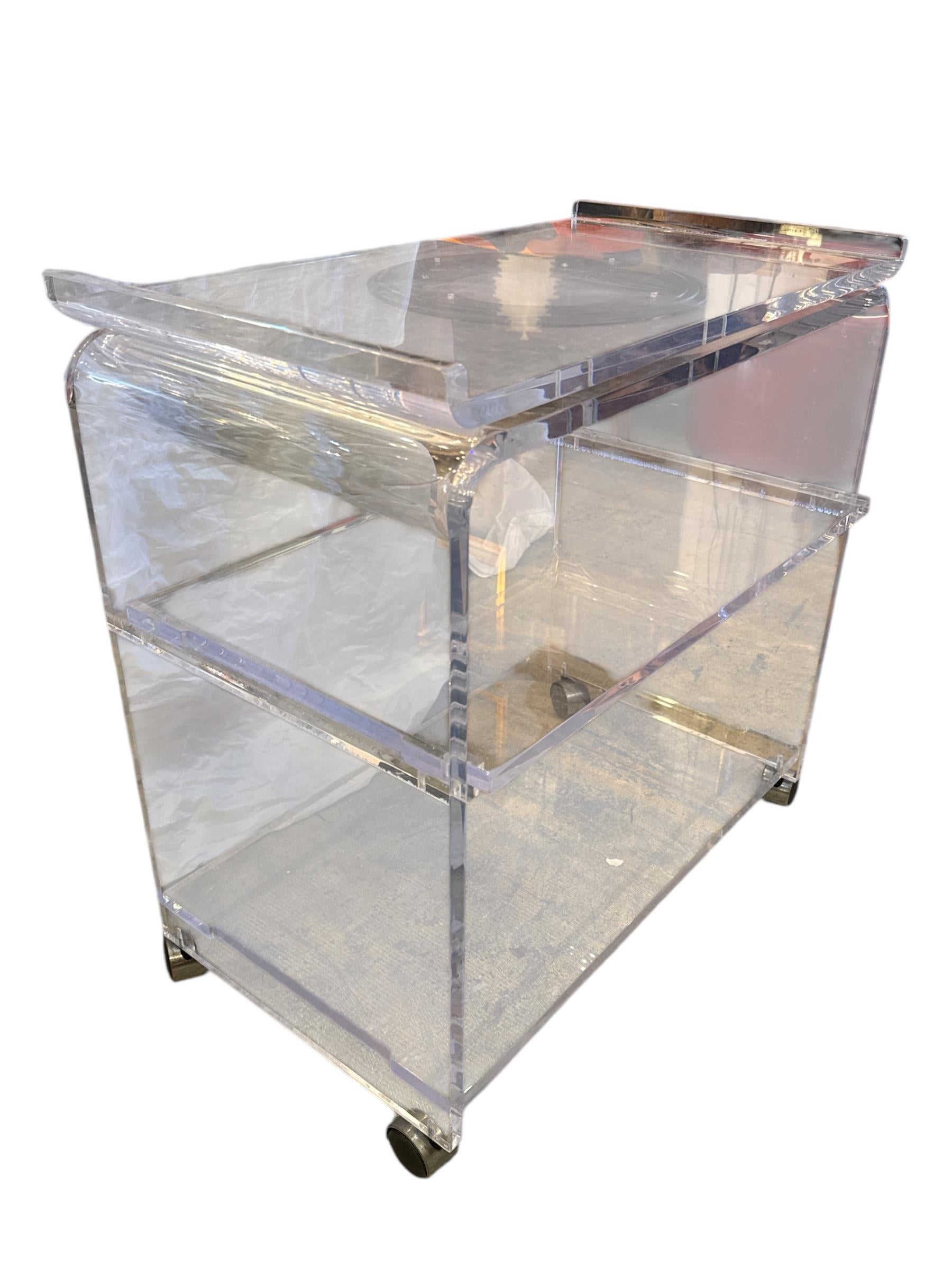 Add a touch of 1970s glamour to your space with this stunning Acrylic Glass Lucite Bar Cart, featuring a sleek, minimalist design and a rotating top for added functionality. This vintage piece is the perfect blend of form and function, making it an