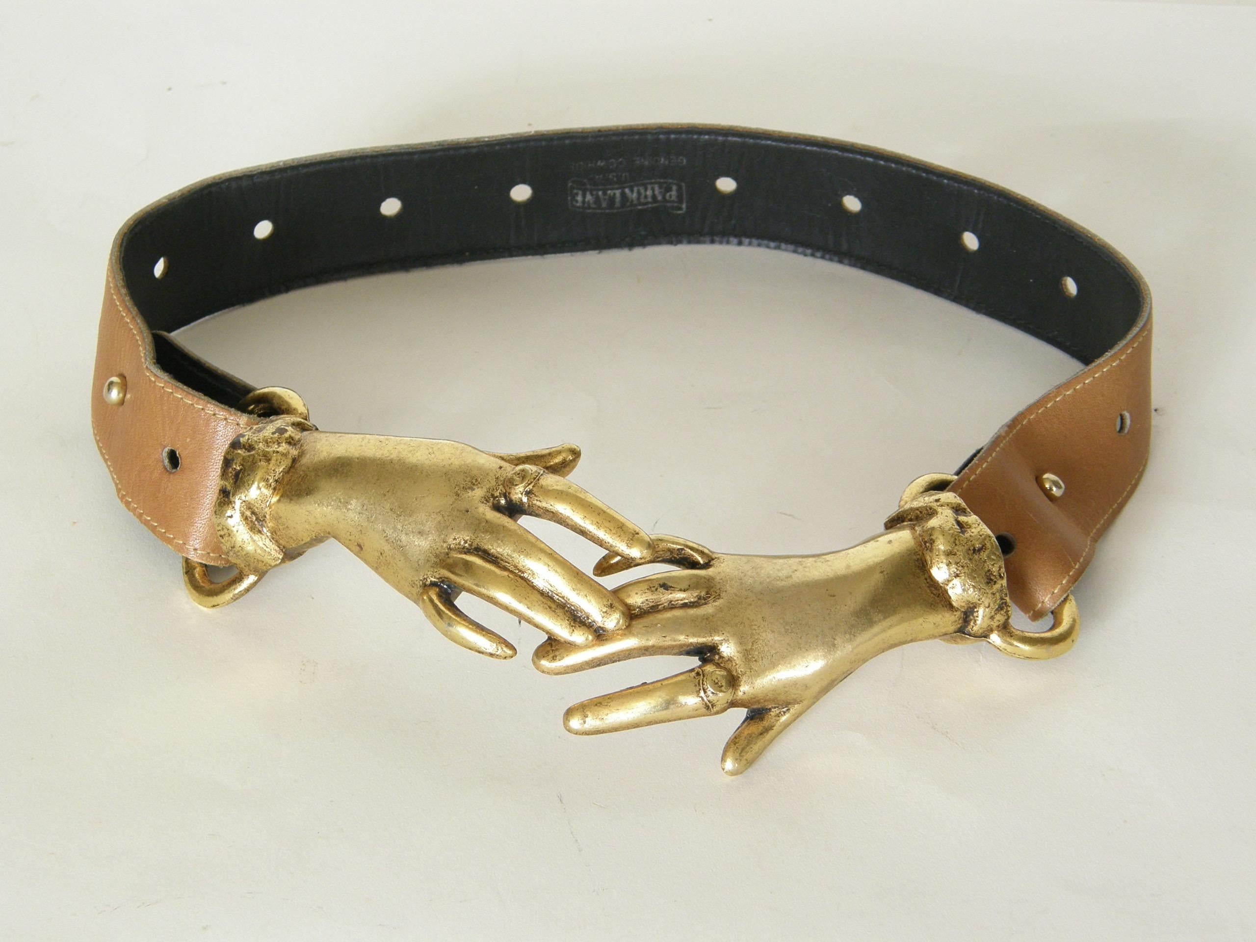 This adjustable belt is a light brown leather and has a charming buckle of two overlapping hands that are not quite clasped. They wear rings and bracelets (or perhaps have fancy cuff details) and have a romantic, Victorian style with an 