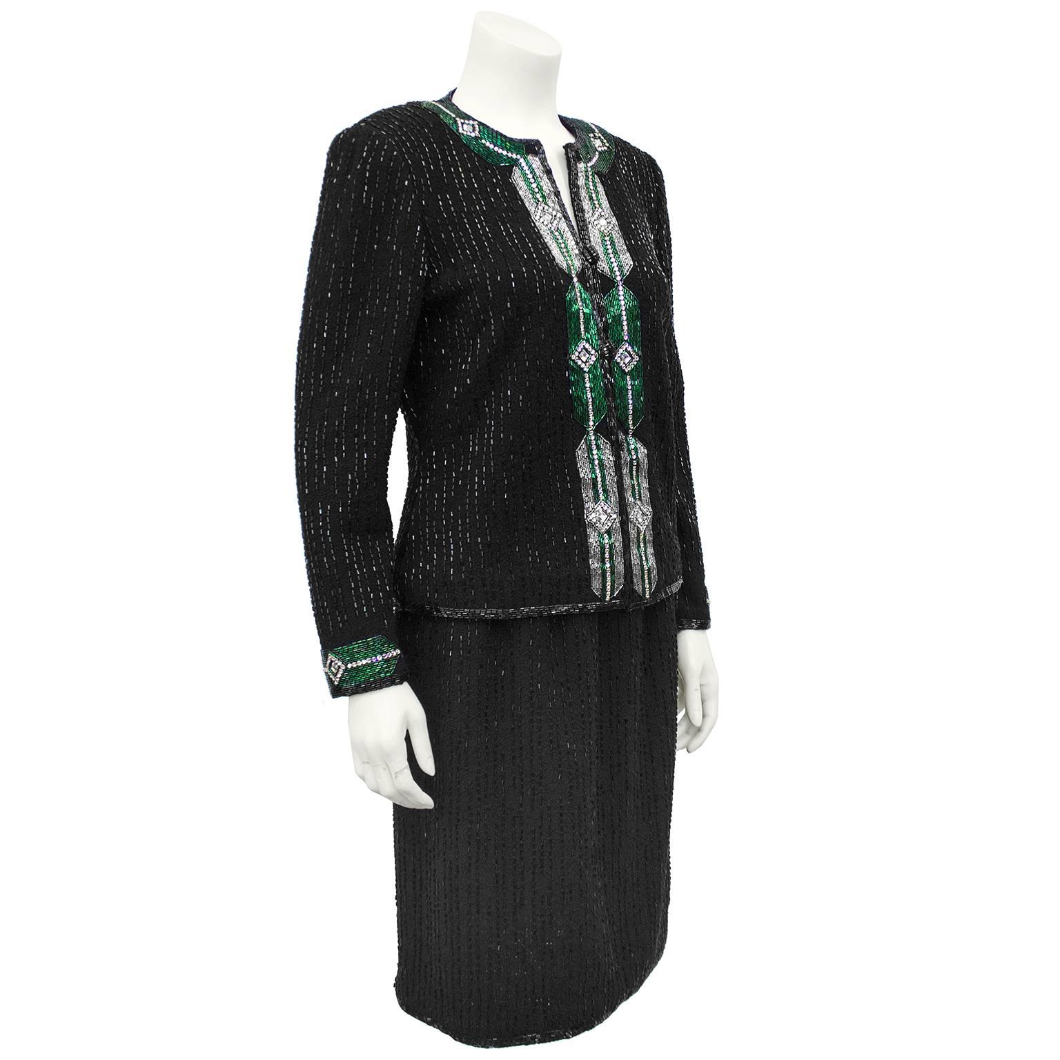 1970s Adolfo black wool knit evening suit. Covered completely in vertical tonal black jet tube beads on both jacket and skirt. Jacket is embellished with stunning silver and emerald green art deco inspired beading at collar, down front and at cuffs.