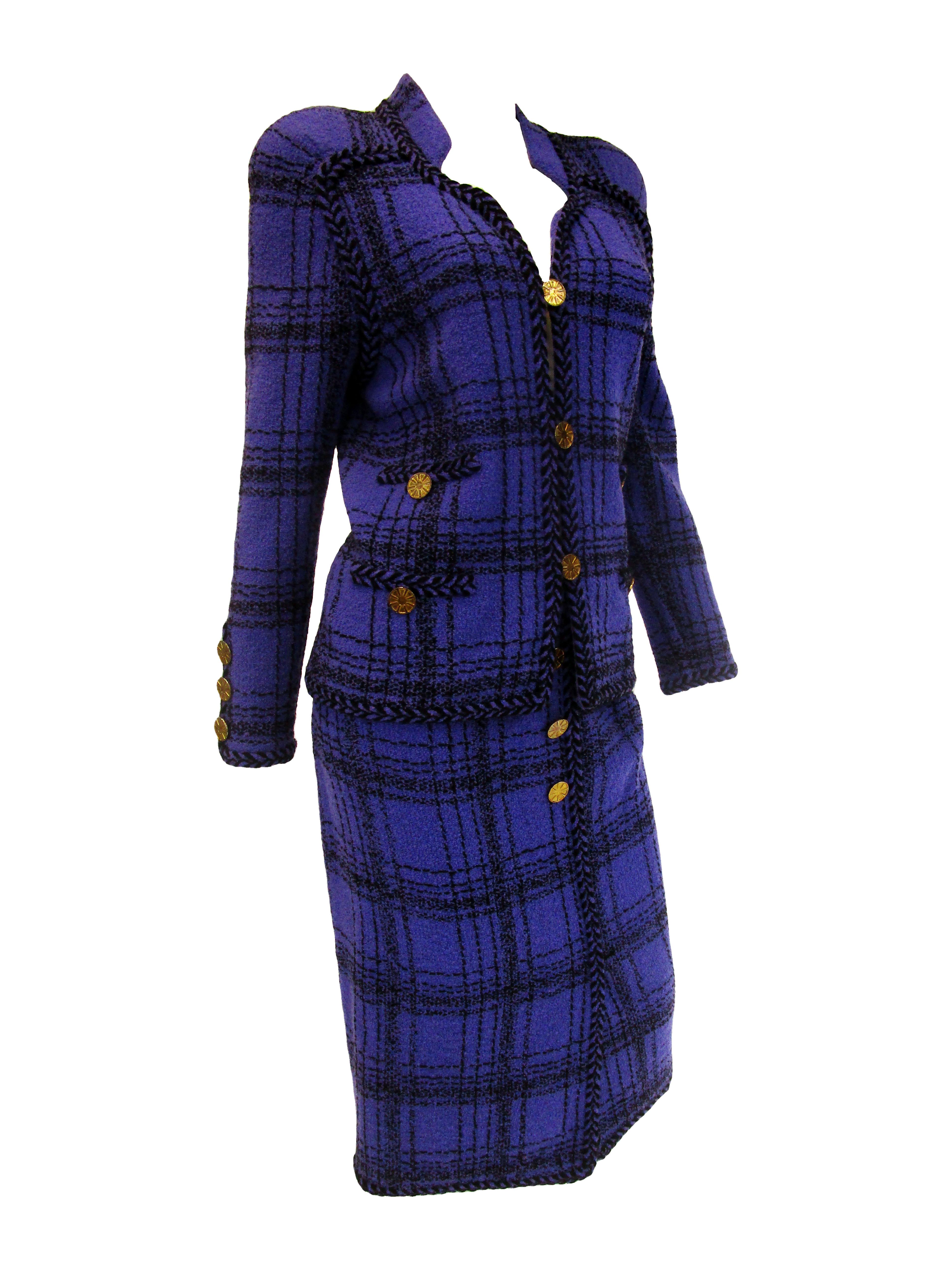 
Take a look at this wonderful wool skirt suit from Adolfo. Purple and black plaid knit fabric make this piece. It features a slightly tailored jacket with broad shoulders and an interesting collar.  A herringbone knit piping and trim that runs the