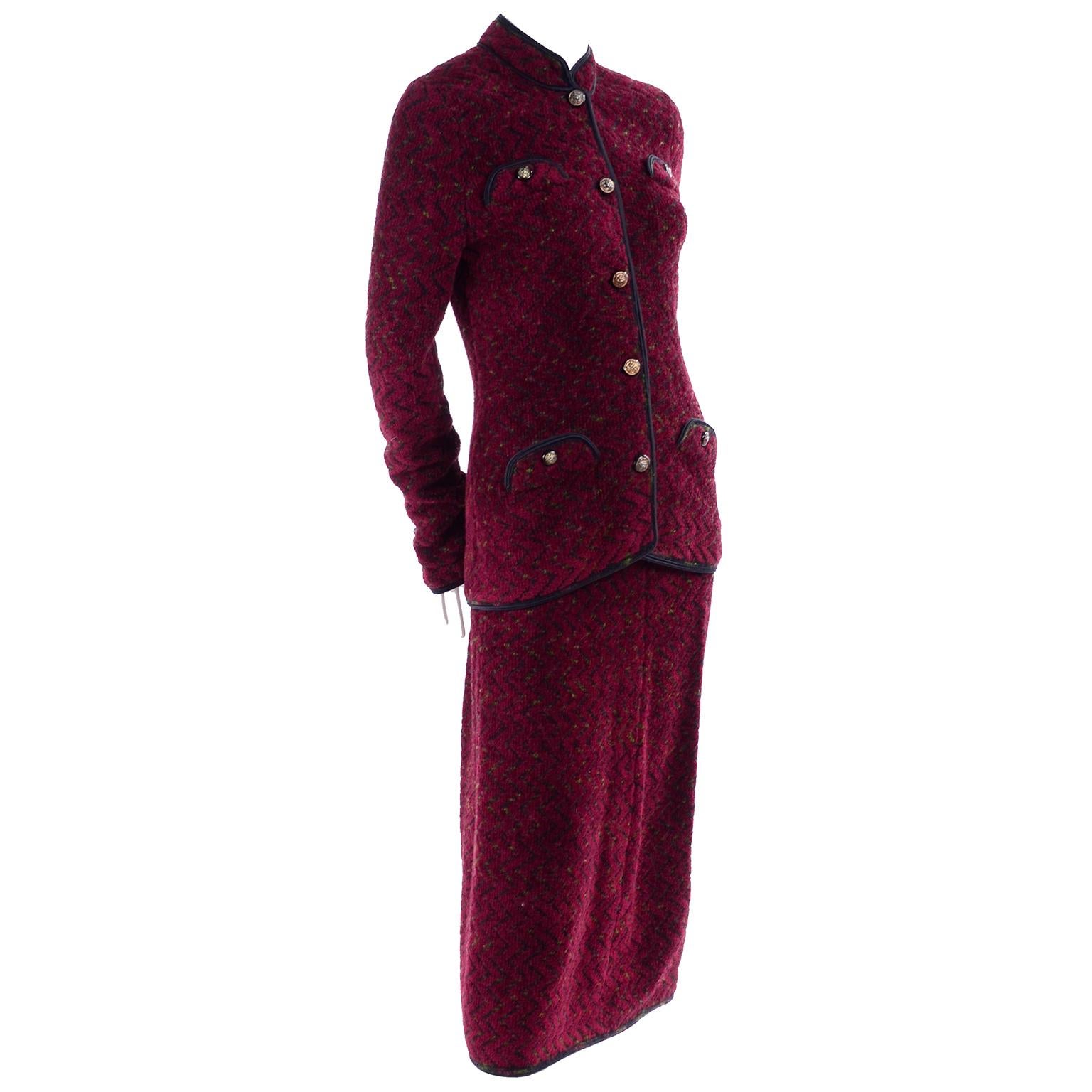 This is a very stylish Adolfo burgundy red skirt suit with a subtle black and green zig zag pattern in the gorgeous knit fabric with black trim. The long jacket has a mandarin collar and 4 decorative inverted flap pockets with lions head brass
