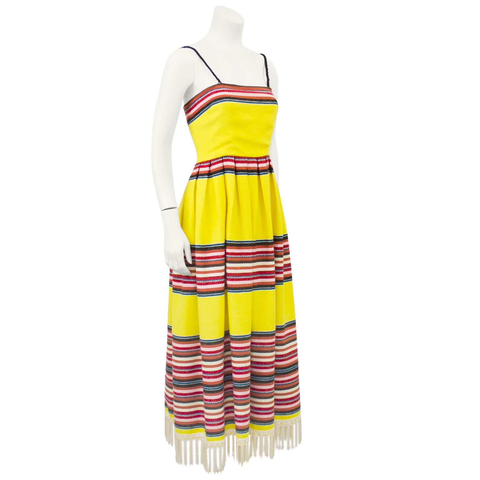 1970s yellow wool blend day gown from the designer Albert Capraro. The pattern on the dress resembles a traditional Mexican blanket with navy, pink and white horizontal stripes along the top of the bust, waist, hips and a large section at the hem.