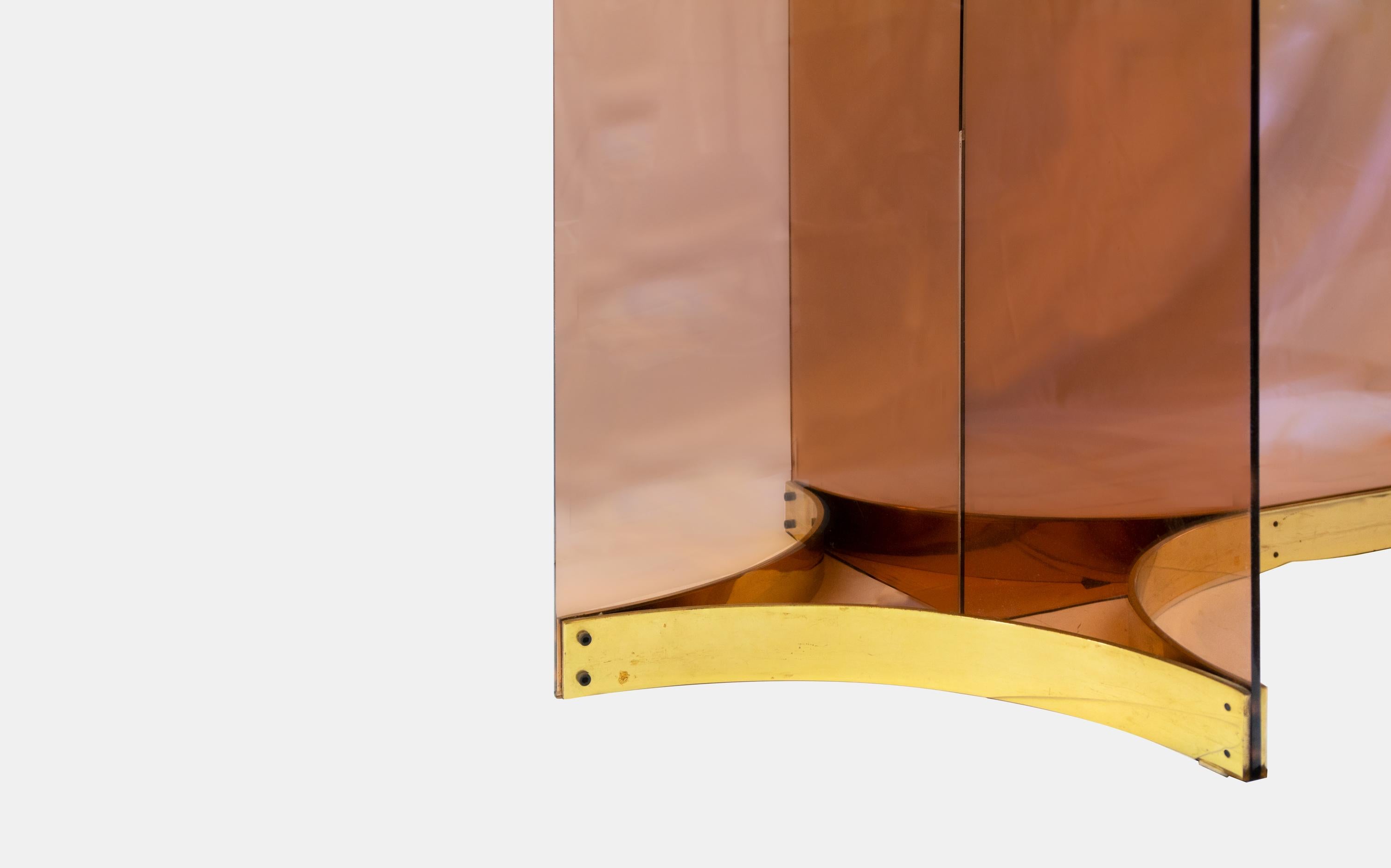 Elegant and sculptural, this Italian dining table from circa 1970 features a striking Perspex base in a sophisticated smoked rose tone, accented with polished brass details. The base supports a generously sized smoked glass tabletop, which is