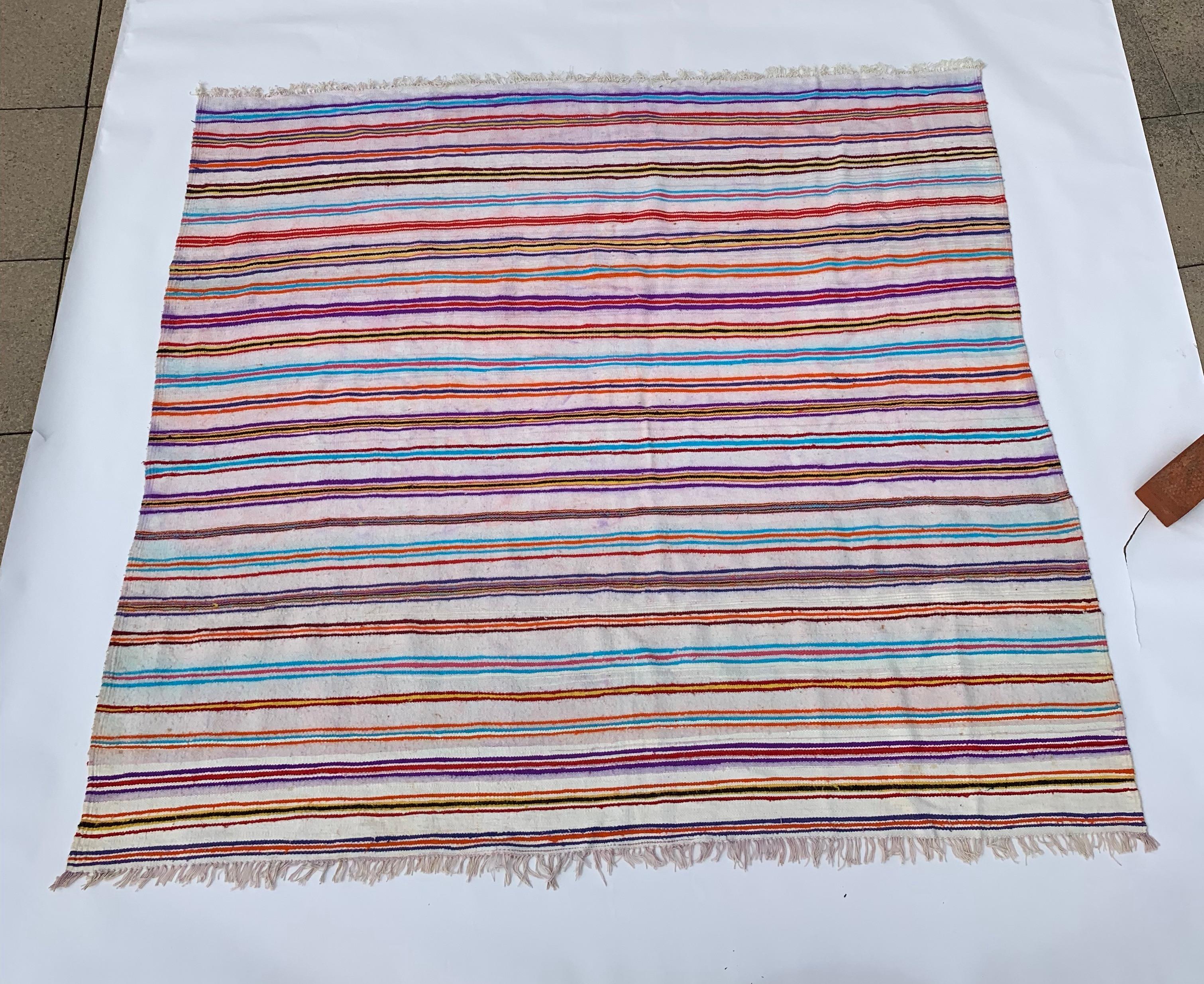 Dieser Berberteppich im Vintage-Stil aus Nordalgerien zeichnet sich durch ein Streifendesign aus, bei dem bunte Streifen in Gruppen auf einem beigen Untergrund angeordnet sind. Mit den Farben Rot, Blau und Violett schafft der Teppich visuelles