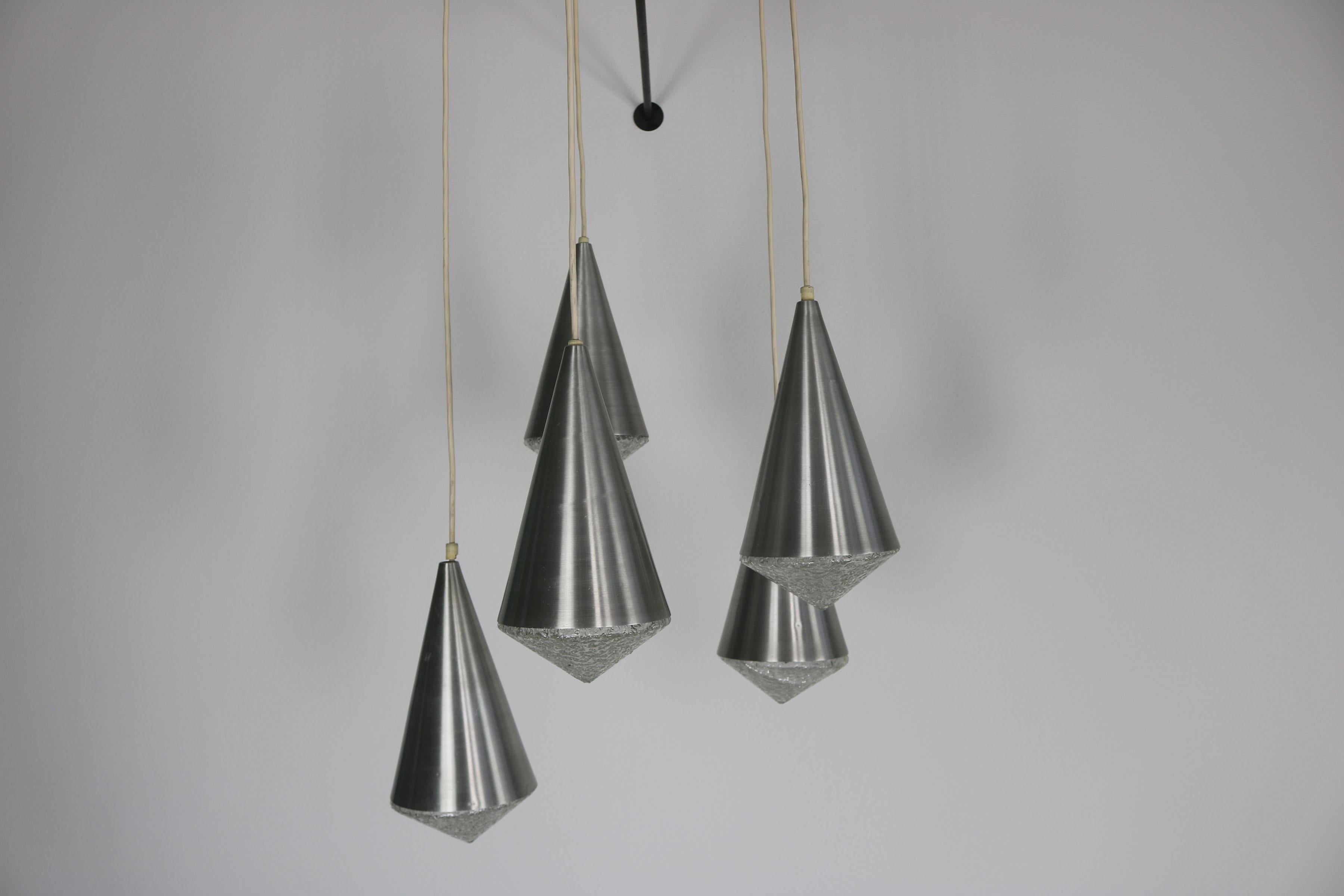 Lampada a sospensione a cascata degli anni '70 con vetro di cristallo
Lampada a sospensione decorativa a cascata degli anni '70, con cinque paralumi a forma di cono in alluminio spazzolato combinati con elementi in vetro cristallo. La struttura a