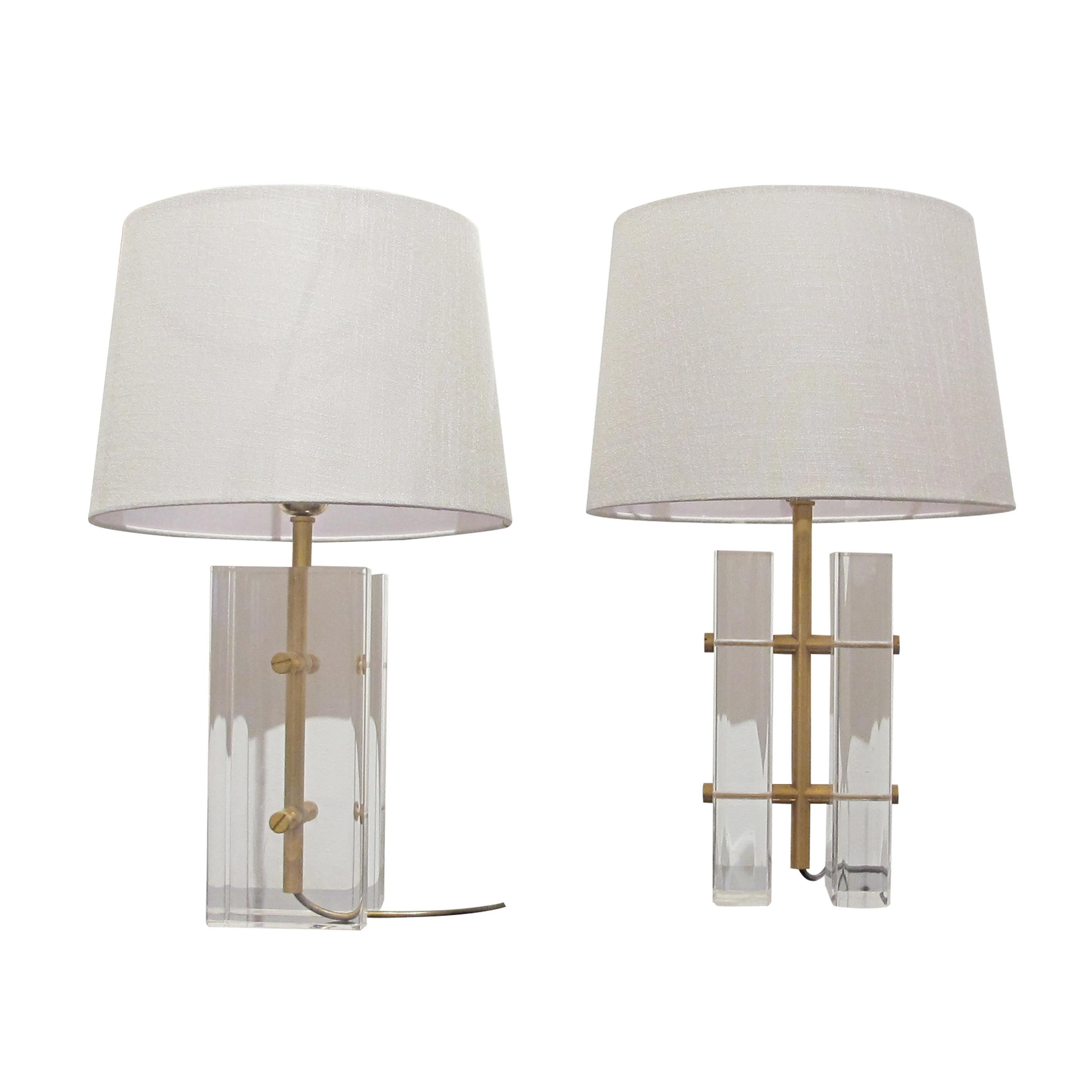 These 1970s table lamps combine clear Lucite blocks with sleek brass accents, creating a striking geometric design. The bases are composed of thick, transparent rectangular pieces of Lucite mounted vertically on a brass framework, giving the lamps