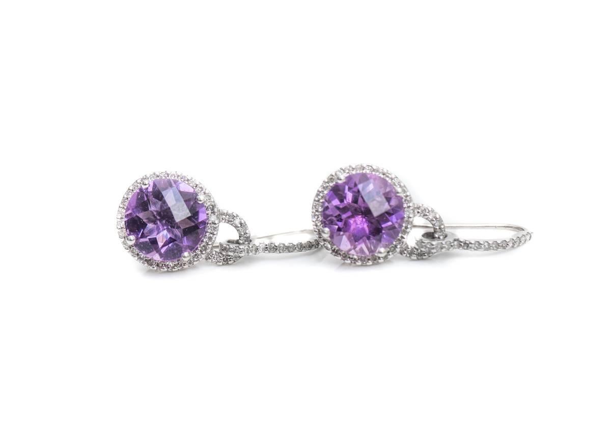 1970s Round Amethyst with Diamond Halo and 14 Karat White Gold Drop Earrings

Each earring features a 10 millimeter, Checkerboard, Round Brilliant Amethyst center stone. A Halo of Round Brilliant Diamonds surrounds the center stone. Diamonds encrust