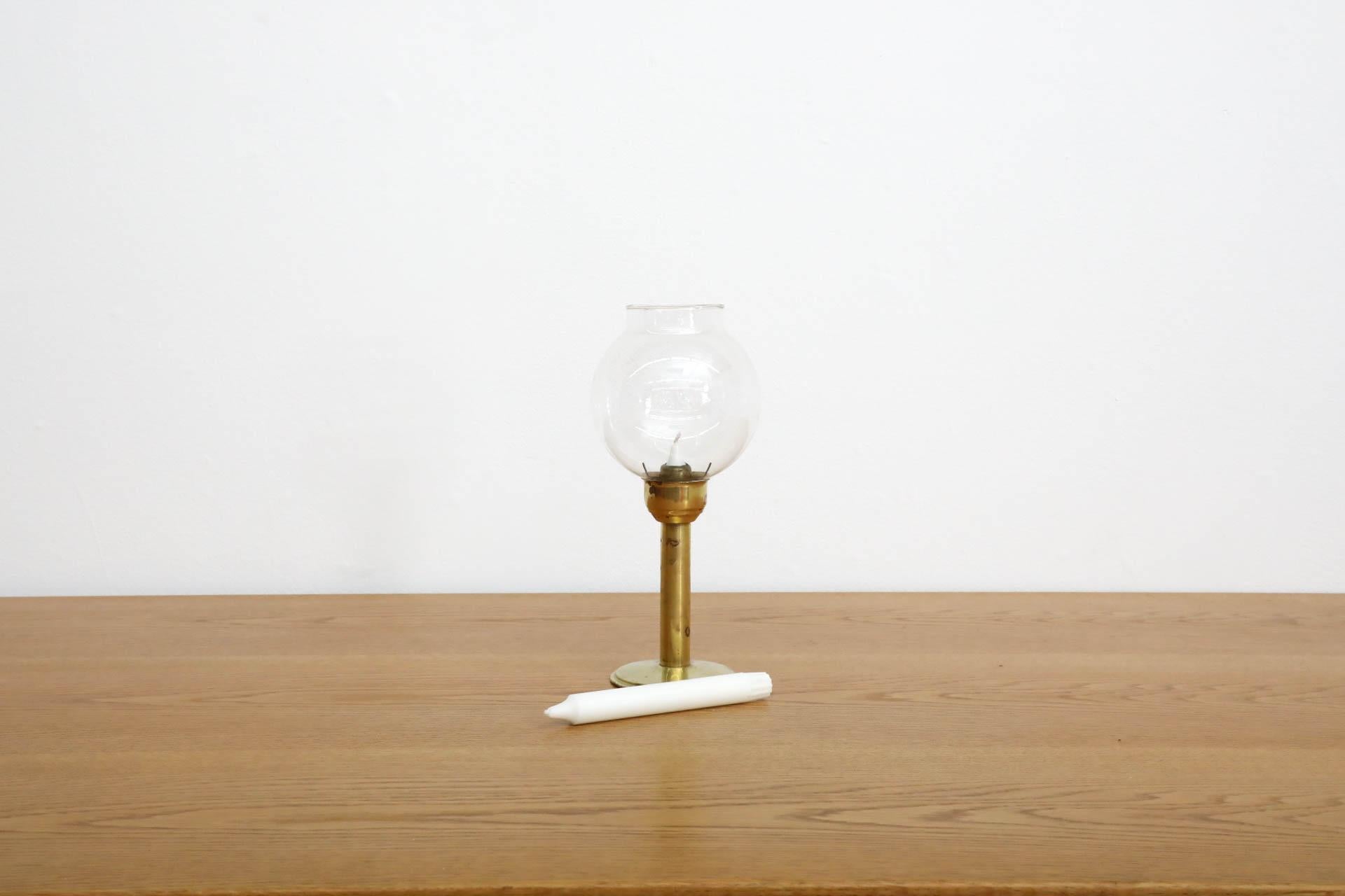 Beautiful, Swedish Mid-Century candle holder from the 1960s-1970s. It features a clear blown glass globe on a brass stand. The candle is placed in the stem and fastened down with a domed cup. As it burns, the inner spring pushes the candle upward. A