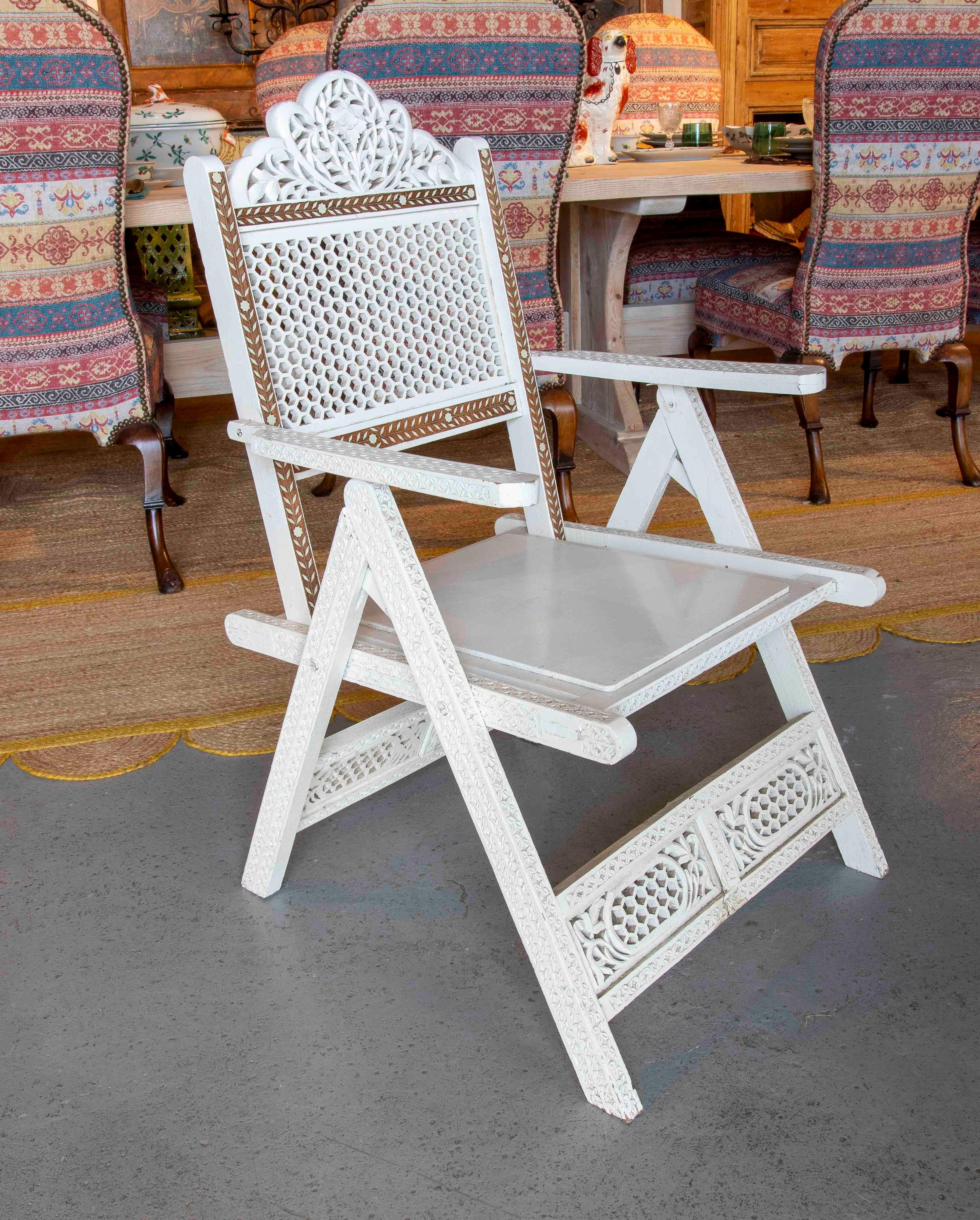 A beautiful Anglo-Indian style folding chair, crafted from hand-carved wood and decorated with intricate bone inlay. The backrest features a geometric openwork design, crowned by an elegant carved floral motif, while the lower crossbar and arms are