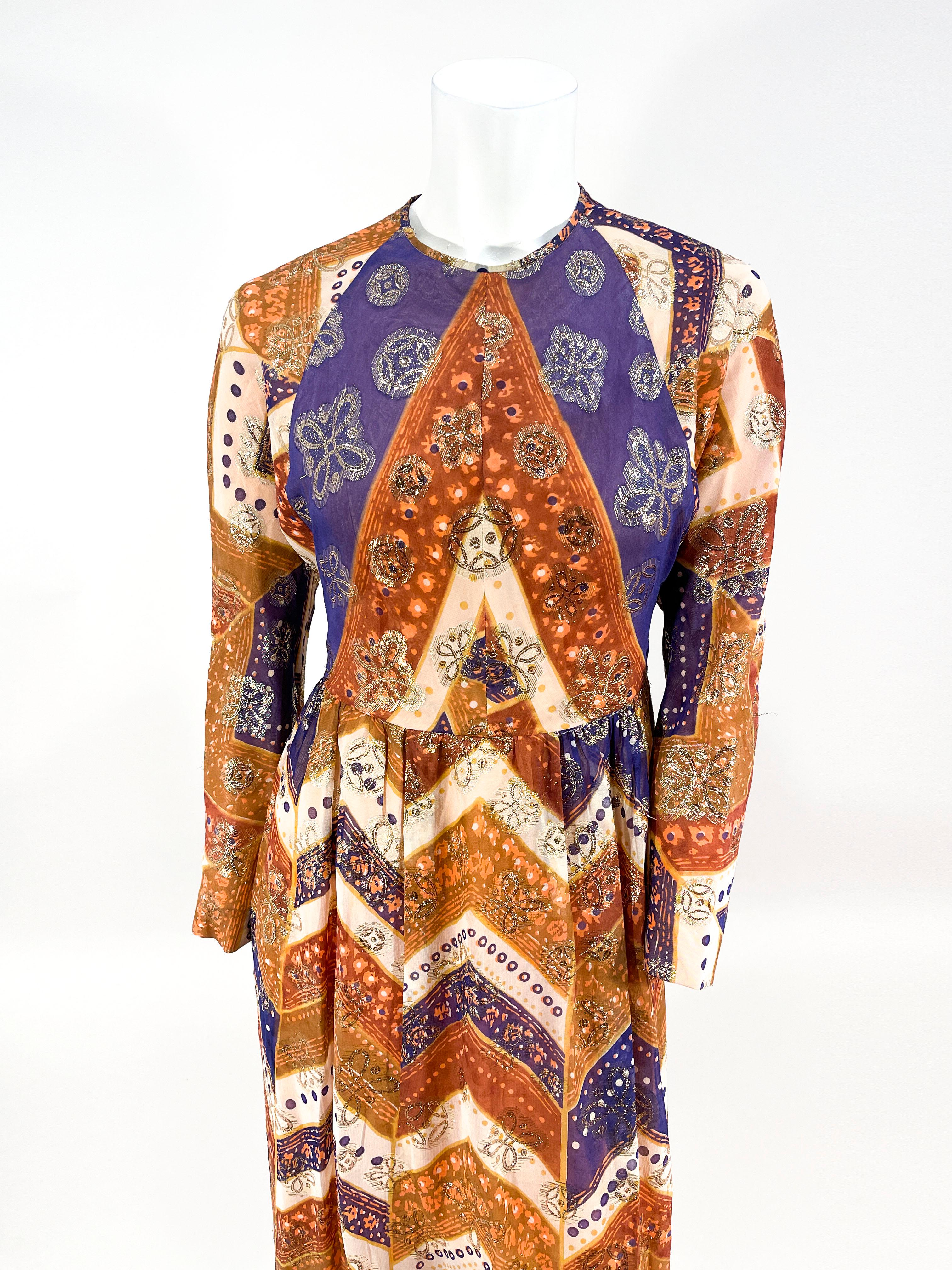 1970s Anthony Muto purple, rust, and beige chevron printed dress. The chiffon textile also features a gold metallic lurex weave in an abstract geometric pattern. The shilouette features a round neckline, long raglan sleeves, a fitted waist, and full