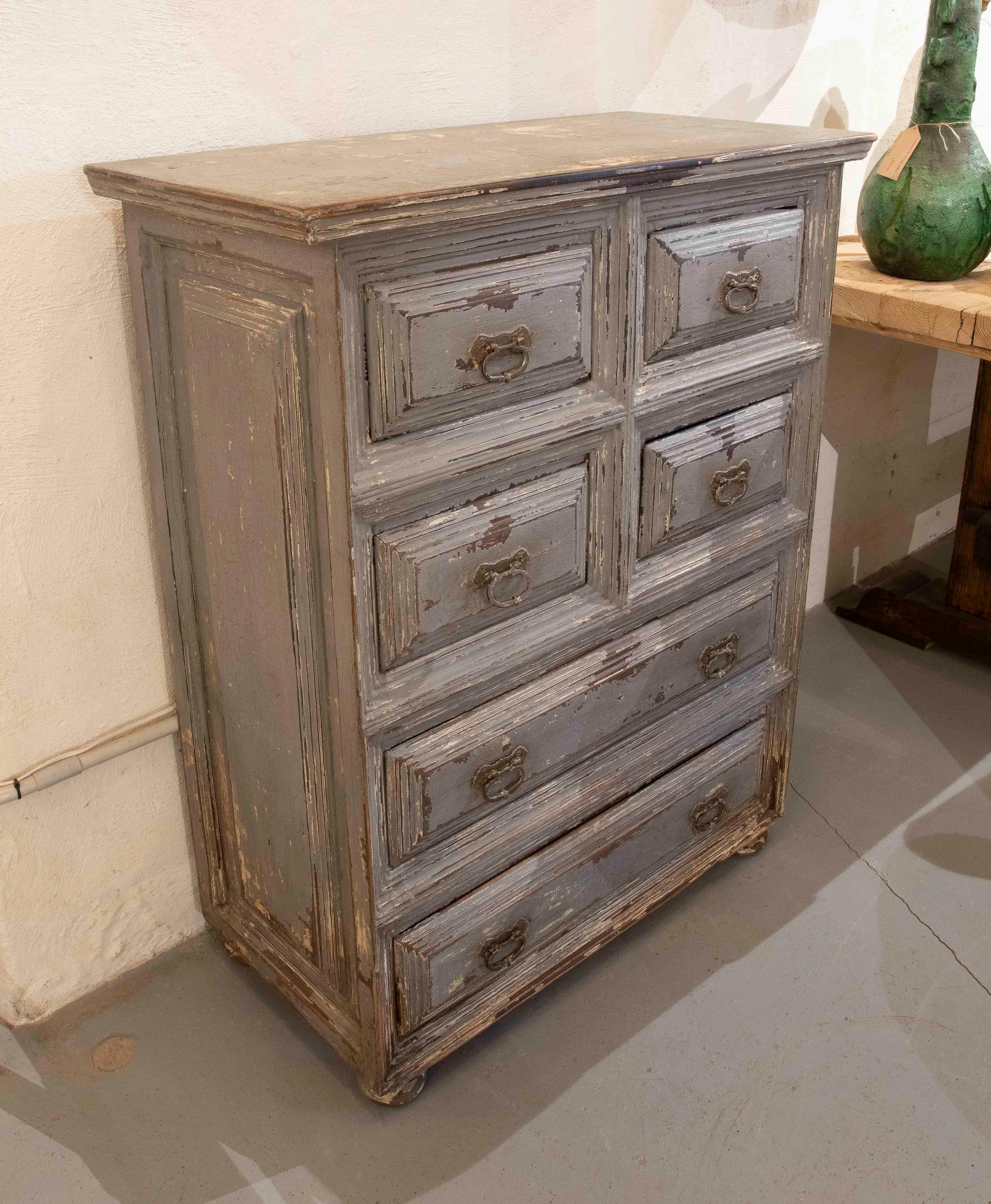 Charme Antiques, cassettiera in legno massiccio con finitura patinata grigia, che rivela gli strati di vernice originali e il passare del tempo. Presenta sei cassetti con modanature intagliate e tiranti ad anello in metallo, che ne preservano